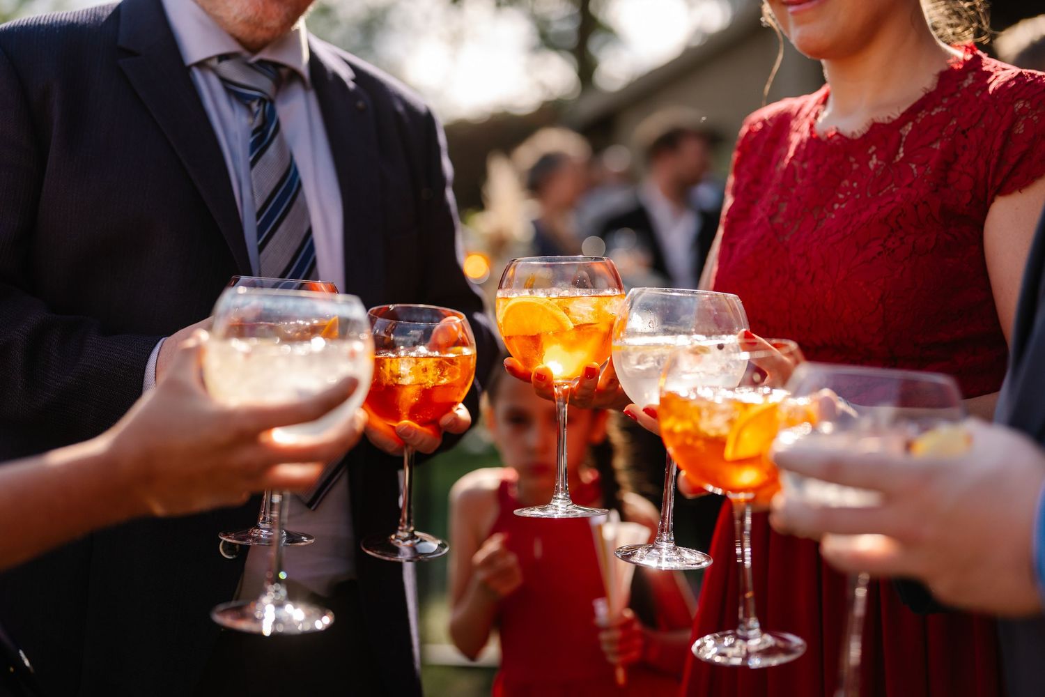 People holding orange cocktails with garnishes at a social gathering or party event.