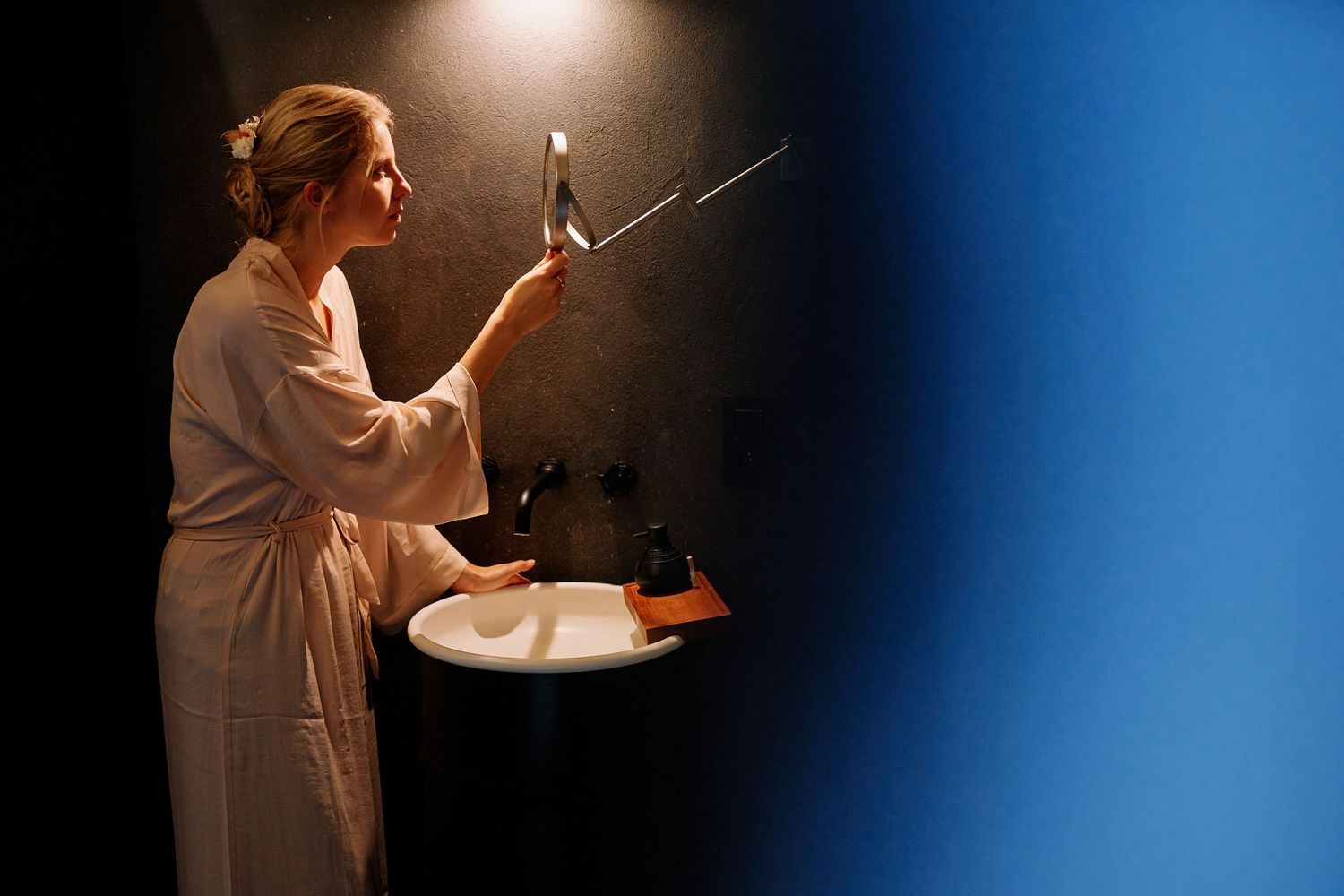 A person in a white robe stands in a dark room holding a candle and matches, creating a dramatic lighting effect.