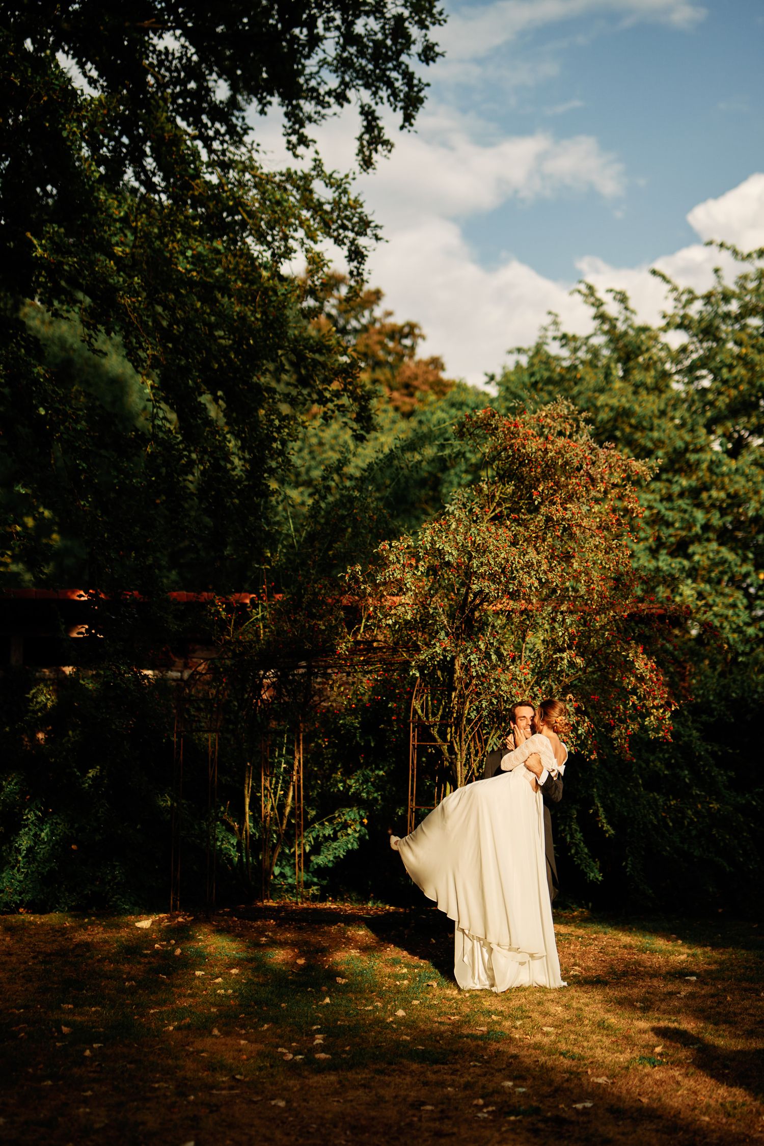 A figure in a flowing white dress stands in a sunlit garden setting at golden hour.