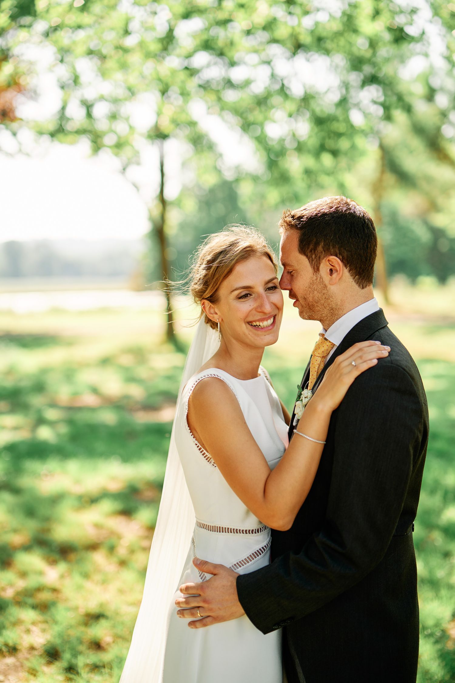 A romantic outdoor wedding moment captured in soft sunlight with greenery in the background.