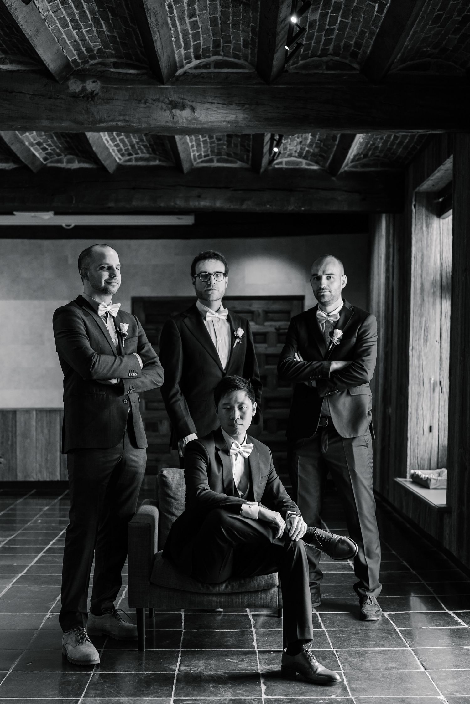 A black and white photo series showing groomsmen posing in a rustic venue with dramatic lighting and shadows.