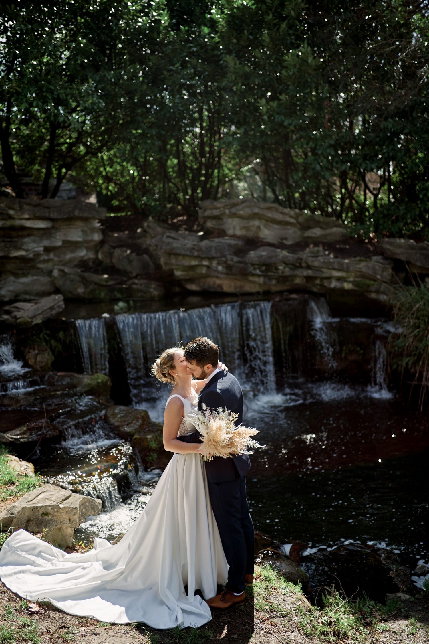 Romantic couple shares intimate moment by scenic waterfall in lush forest setting.