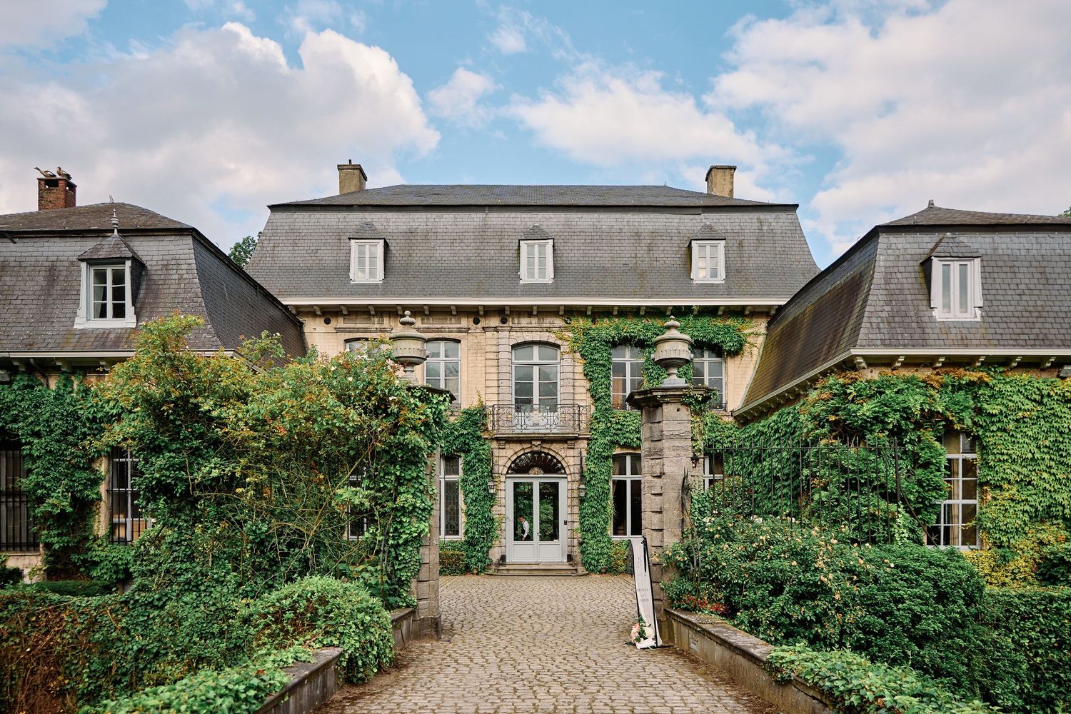 A panoramic view of a rustic French country estate with stone buildings and lush green gardens along the courtyard.