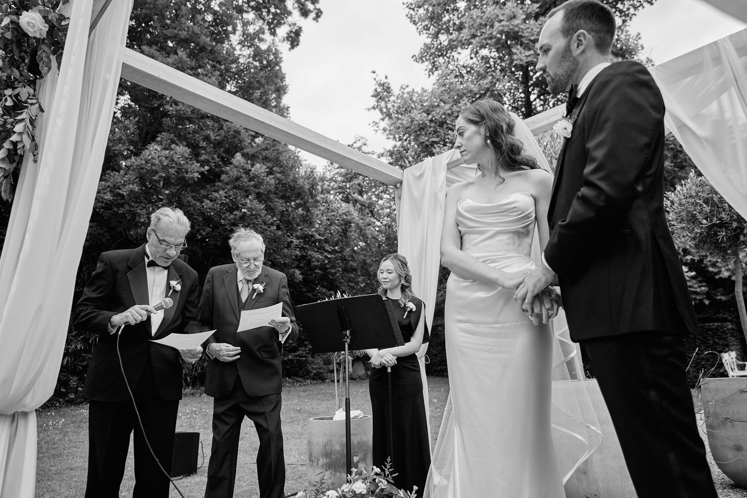 A series of black and white wedding photos showing candid moments between couples and guests during an outdoor ceremony.