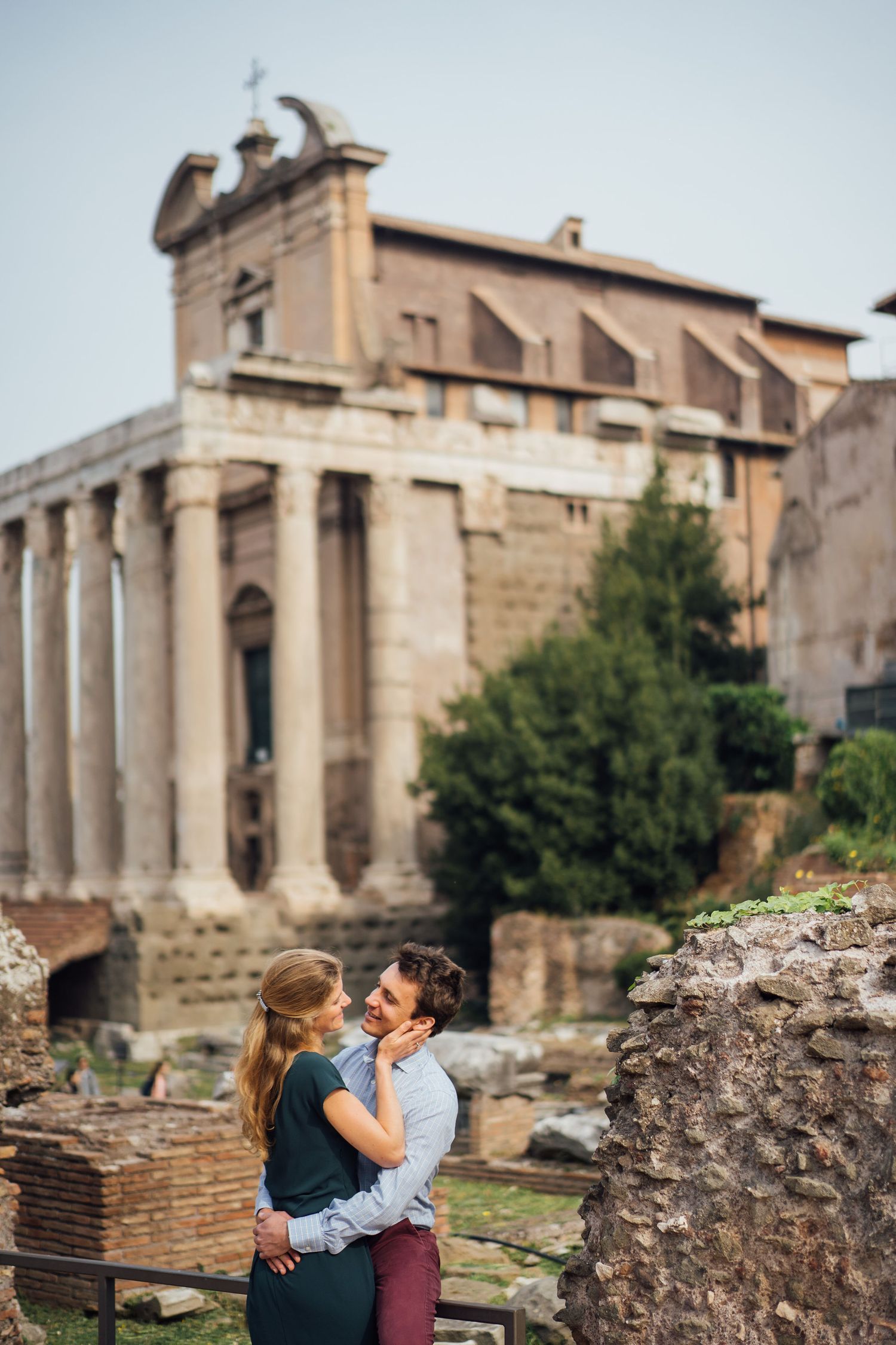 A romantic couple embraces near ancient Roman ruins and stone columns in the historic Forum of Rome.