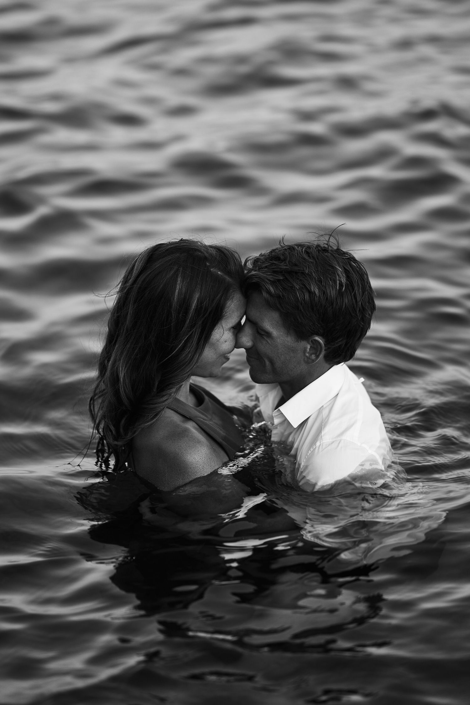 Two people share a romantic kiss while partially submerged in rippling water, captured in black and white.