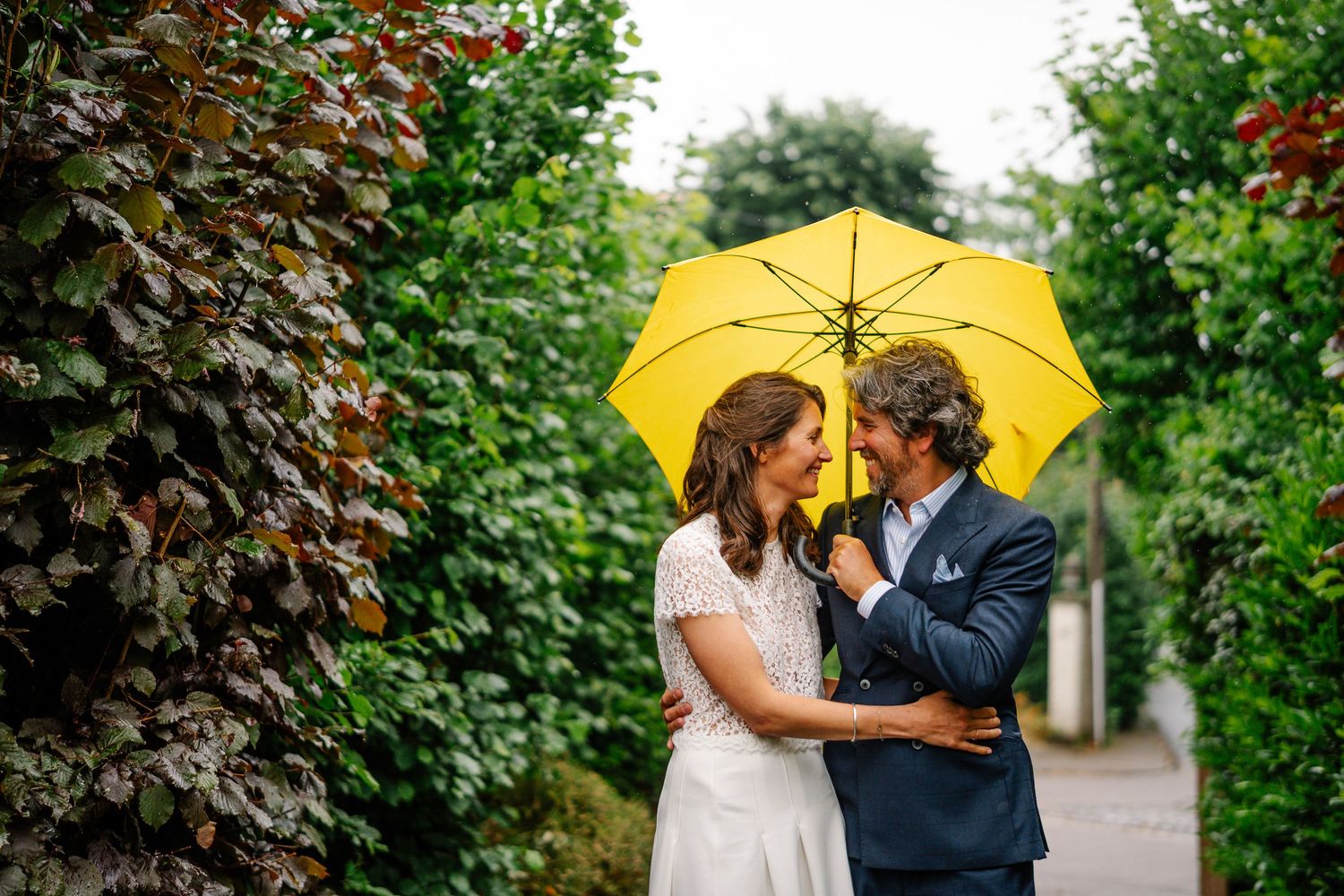 Couple sharing an intimate moment under a yellow umbrella in a lush garden setting.