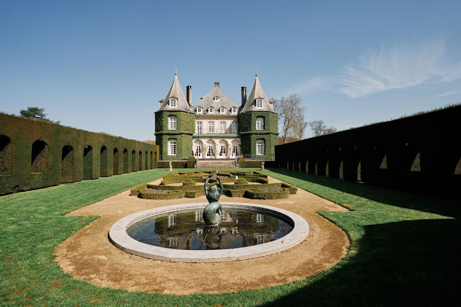 Panoramic view of an ornate garden fountain surrounded by manicured hedges and circular pathways at a historic estate.