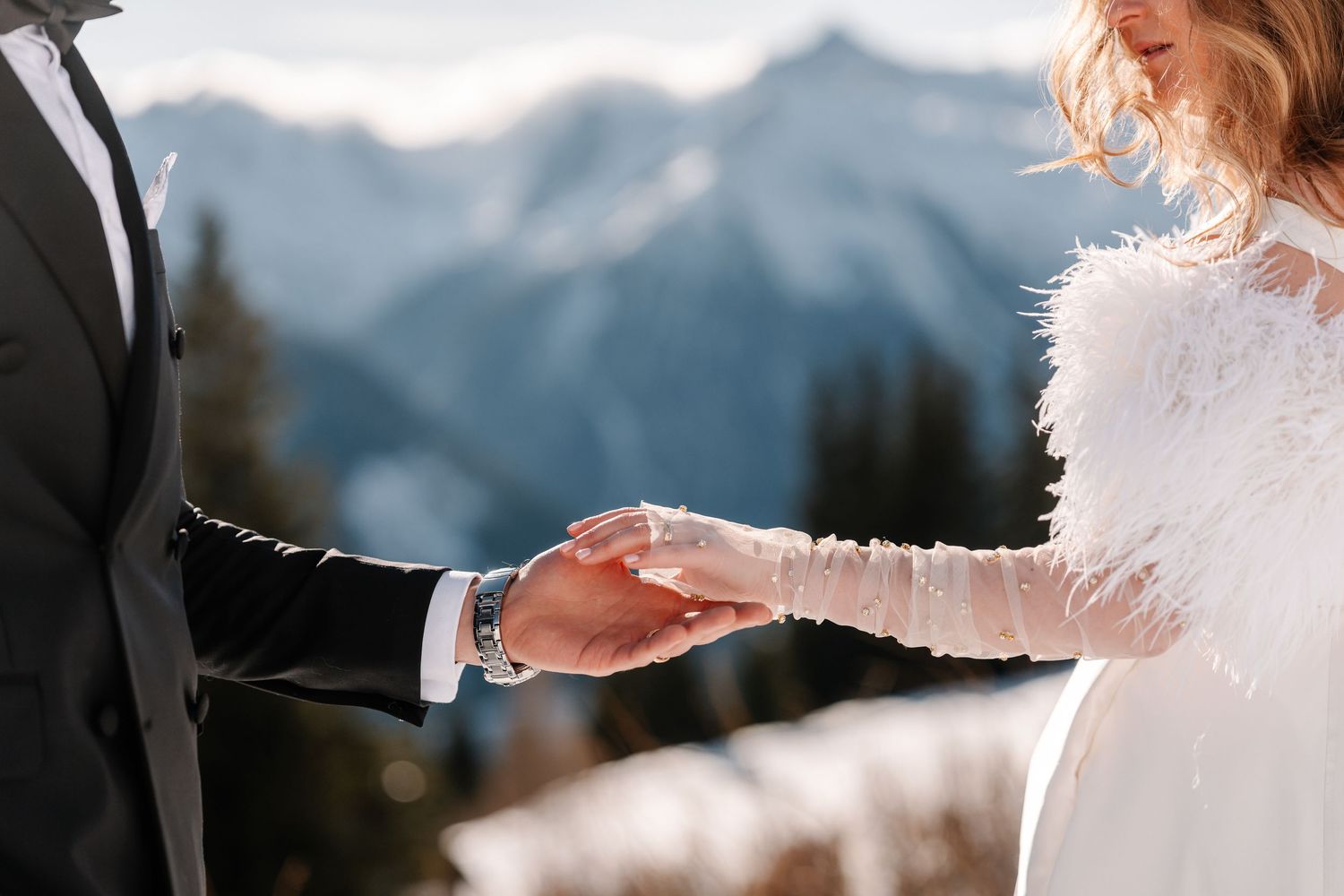 A romantic wedding couple holds hands during an outdoor mountain ceremony with soft lighting and elegant attire.