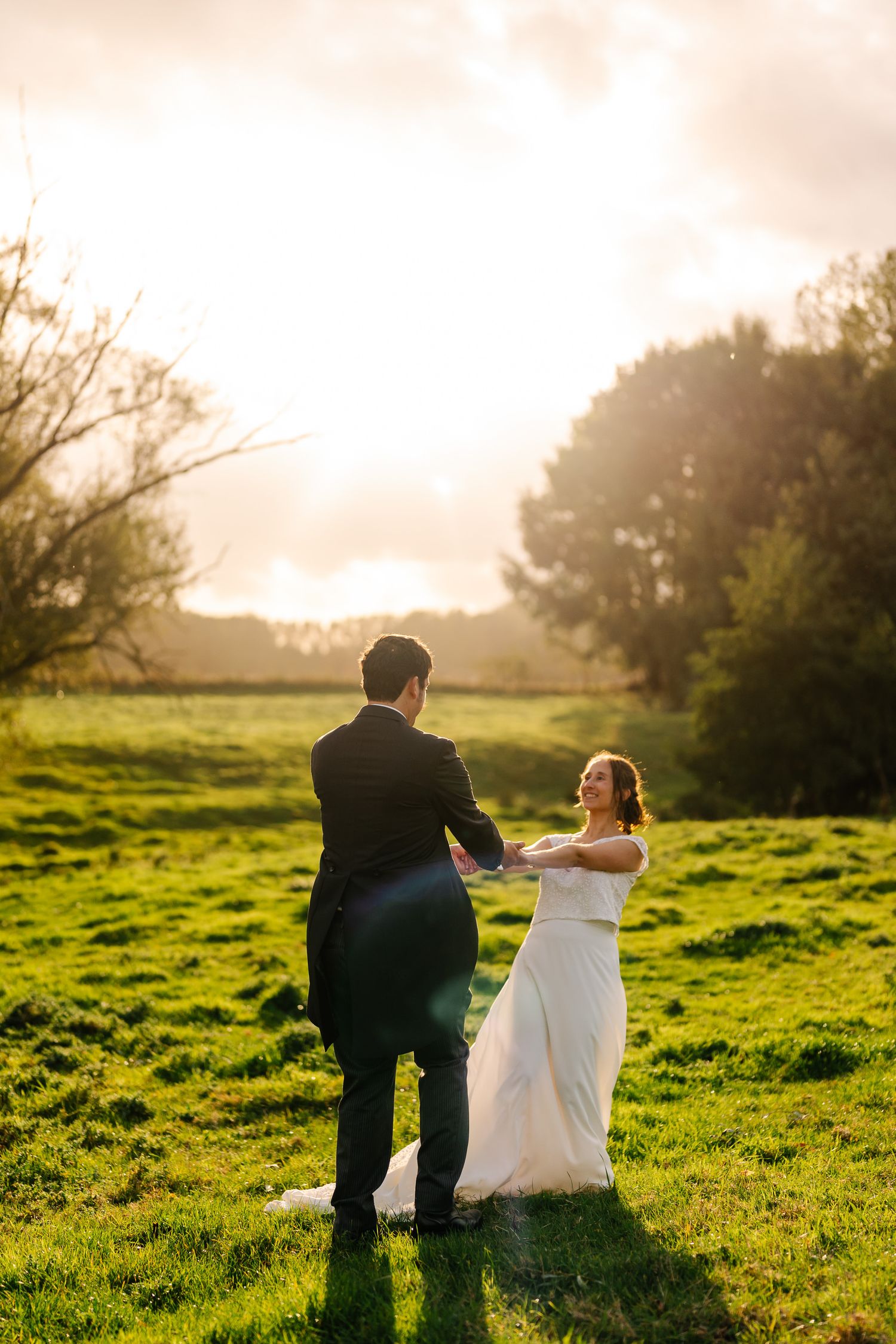 A couple sits together on a grassy hillside during golden hour sunset in a romantic outdoor setting.