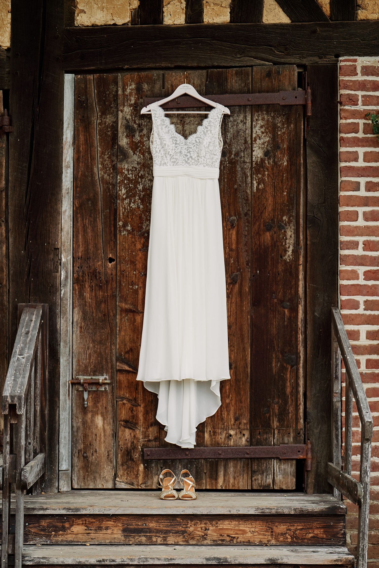 White wedding dress and shoes displayed on rustic wooden barn wall with brick accents.