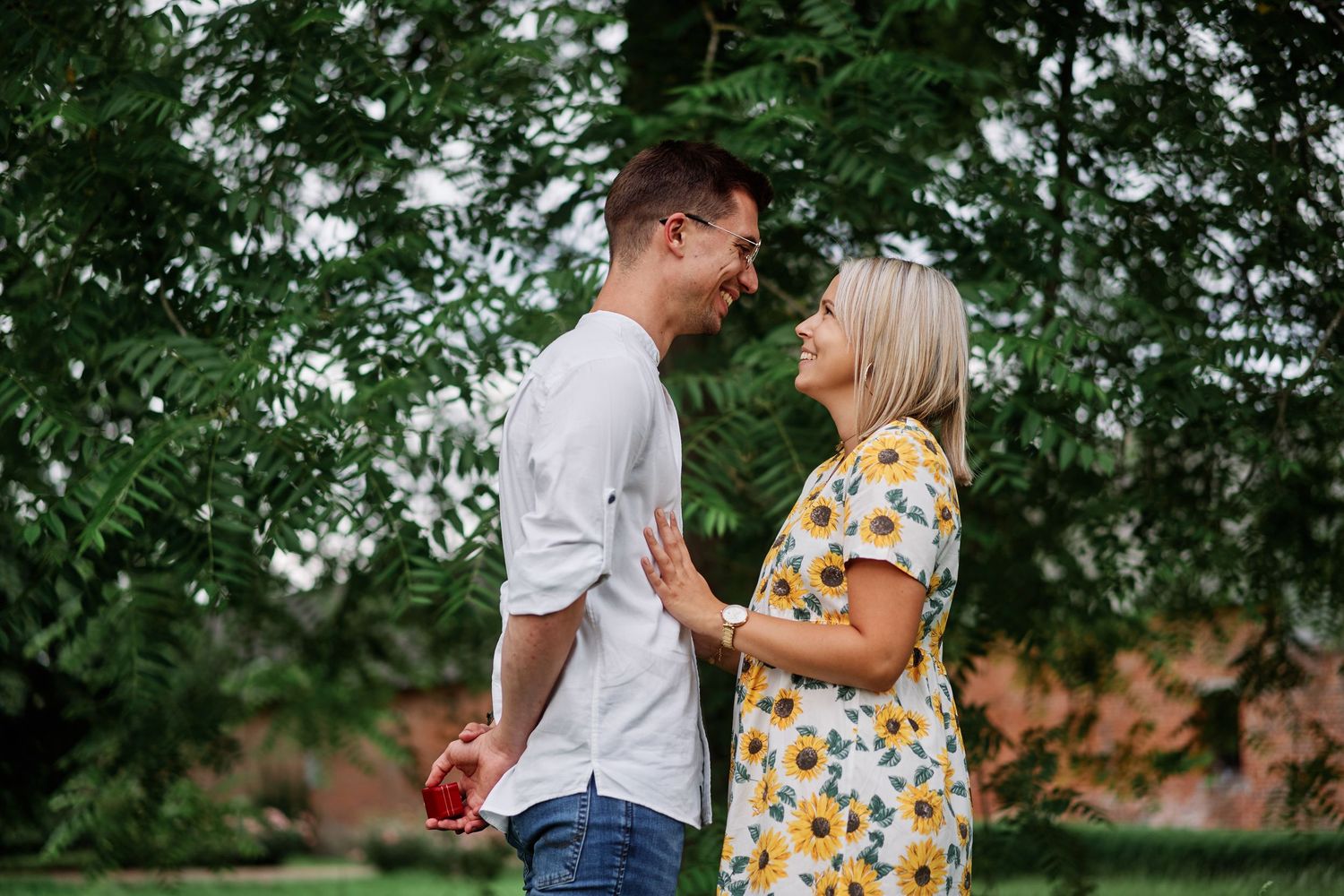 A couple shares a tender moment in a garden setting with green foliage in the background.