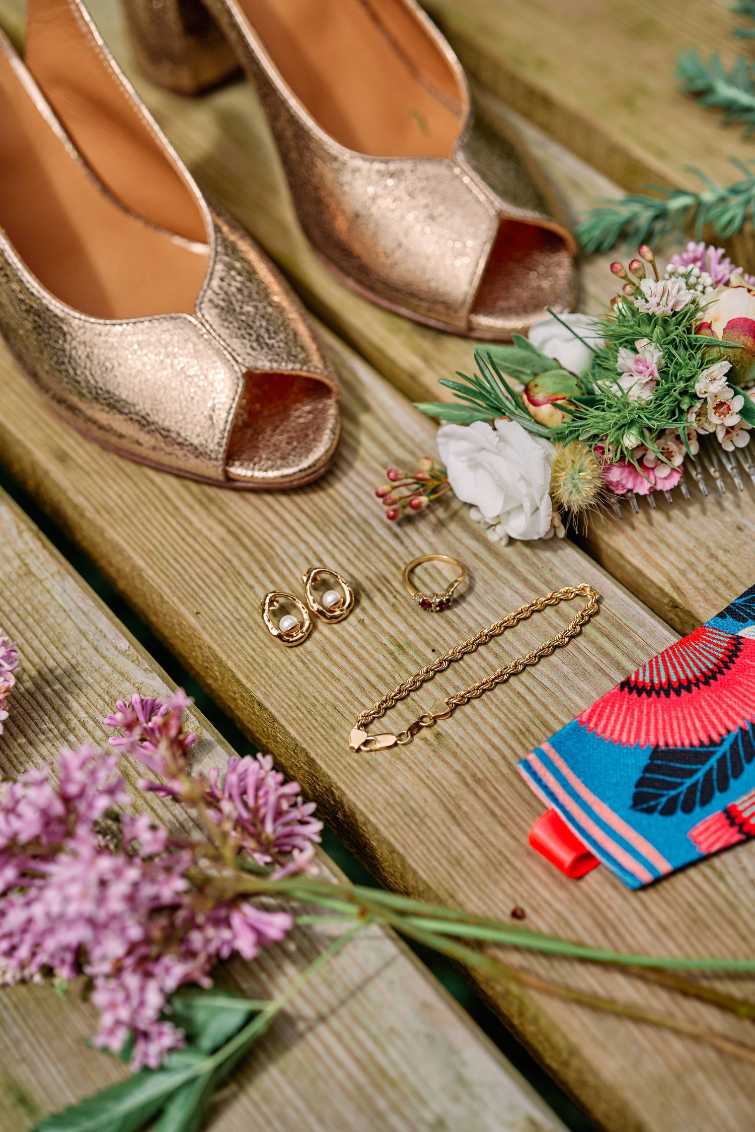 Wedding accessories including sparkly shoes, rings, and pink flowers arranged on rustic wooden planks.