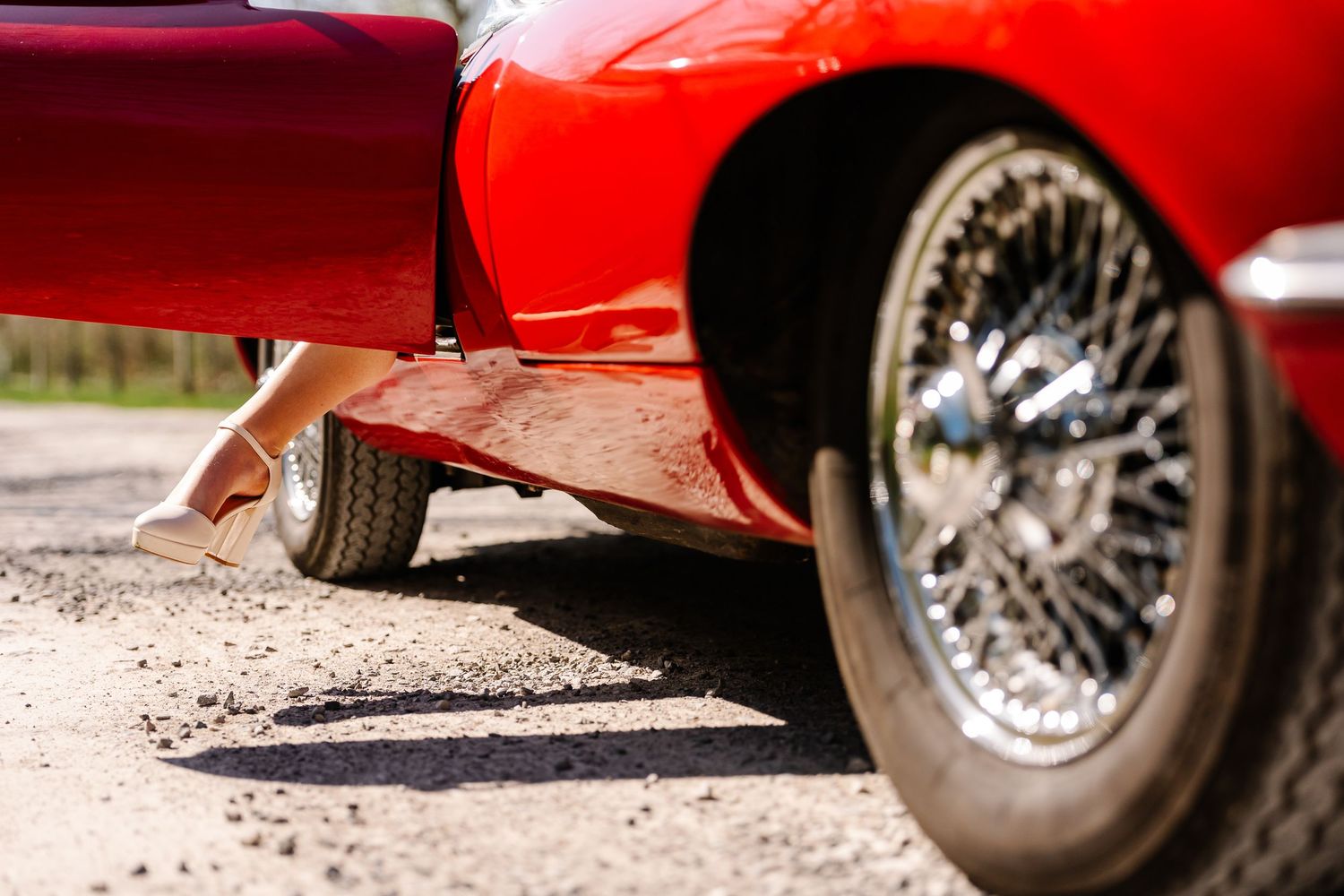 Close-up view of a bright red vintage car's chrome wheel and low-profile tire against a gravel surface.