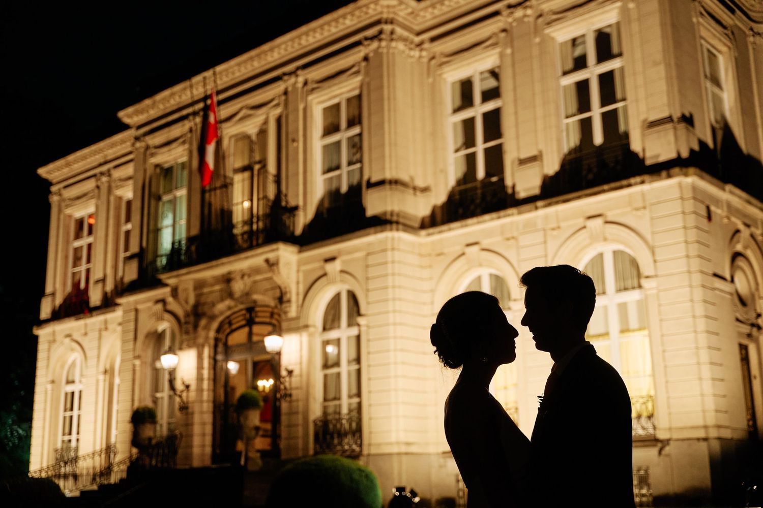 Silhouetted figures stand in front of an illuminated historic building facade at night creating a romantic ambiance.