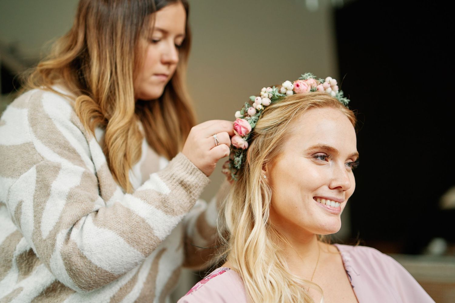 A wedding day preparation scene showing a floral crown being placed on long blonde hair.