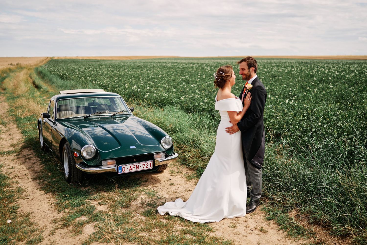 A classic teal convertible car parked in a lush green farm field during a summer day.