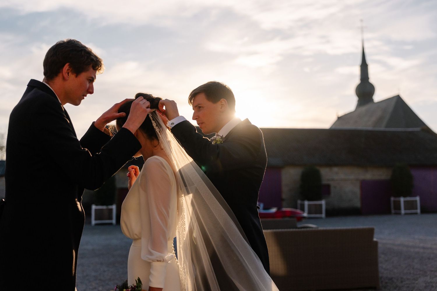 A couple shares a romantic kiss at sunset with a church steeple silhouetted in the background.