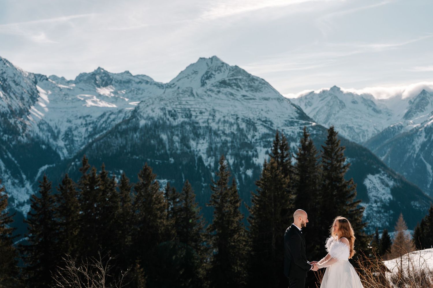 Snow-capped mountain peaks rise above evergreen forests in a dramatic winter landscape.