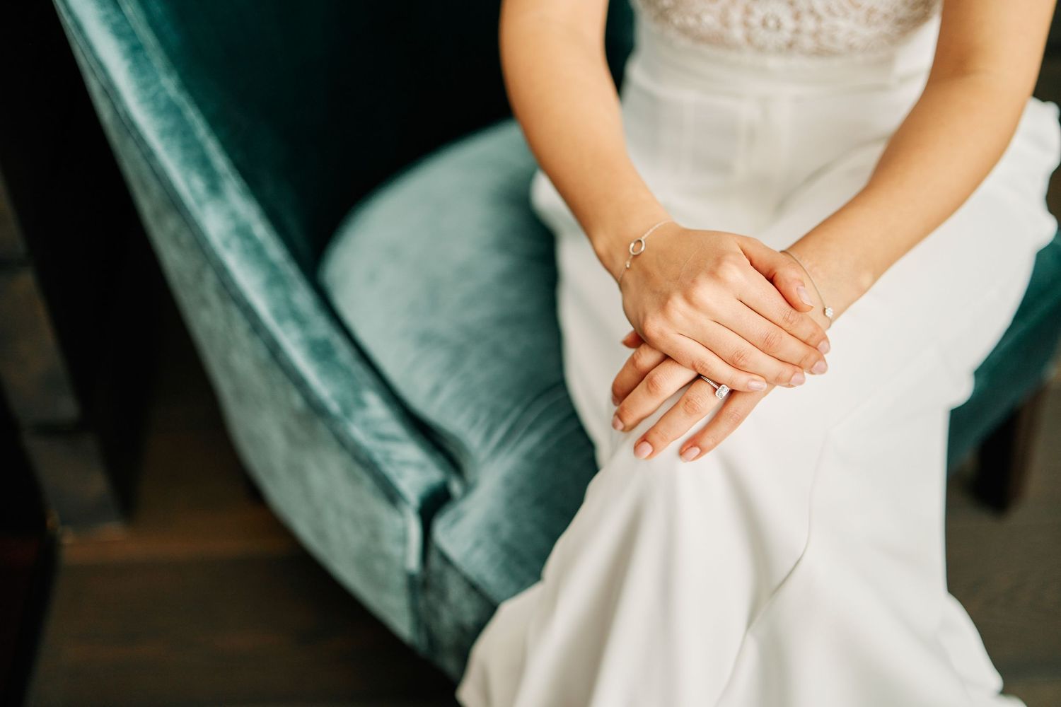 A close-up detail shot of hands resting on a white wedding dress with delicate lace and beading details.