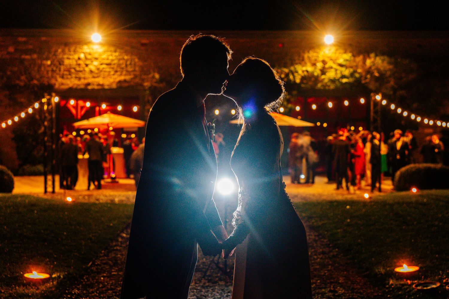 Silhouettes of couples dancing under warm string lights and lanterns at an outdoor evening celebration.