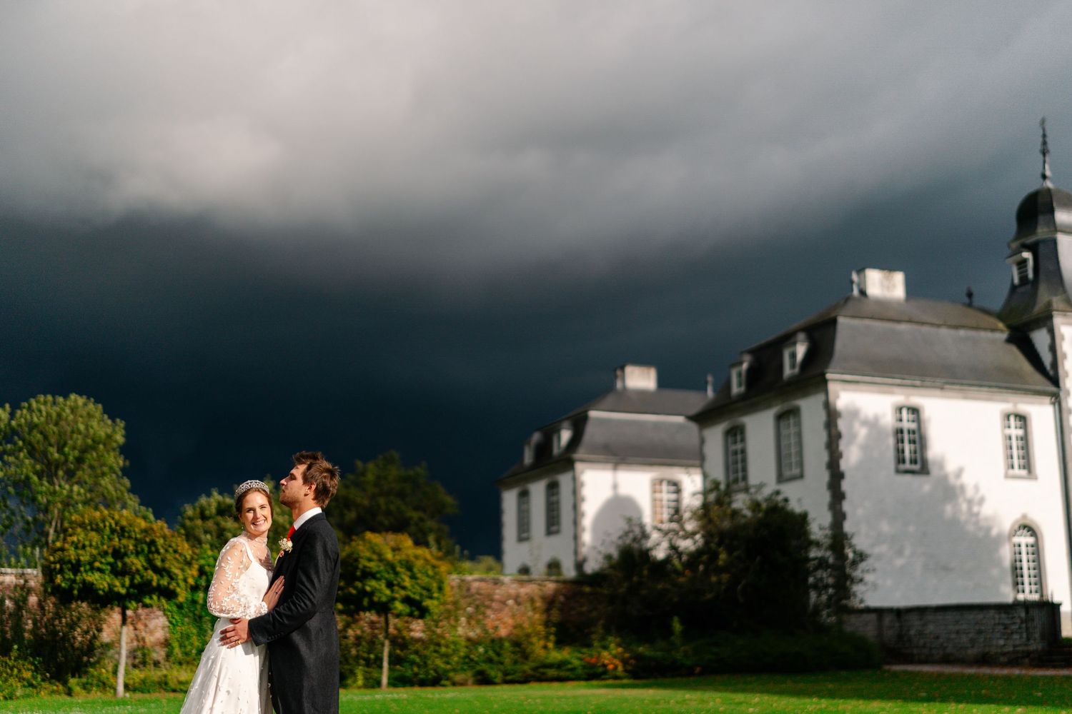 Storm clouds gather behind a white church building and steeple in dramatic evening light.