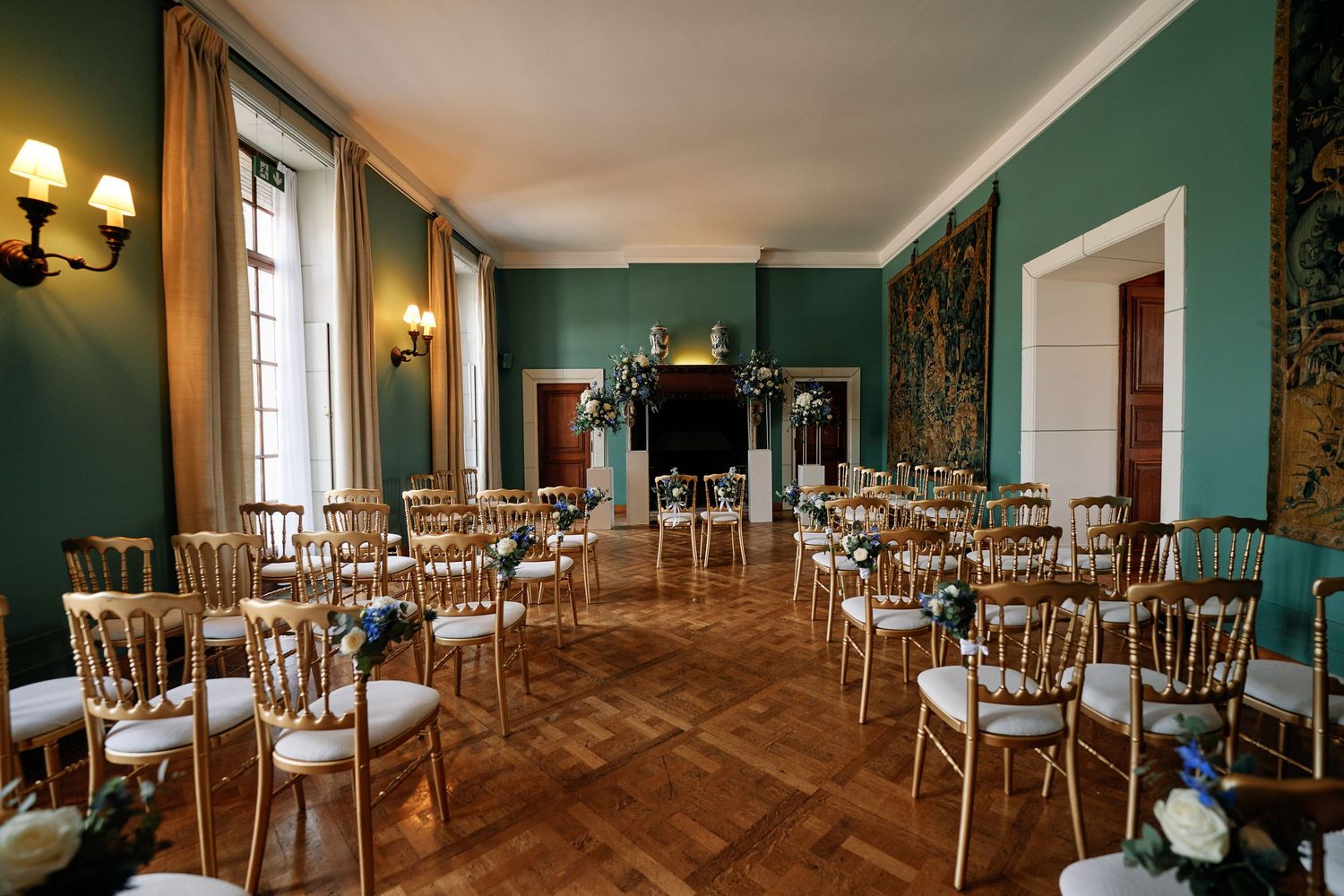 Elegant dining room with turquoise walls features rows of wooden chairs and tables illuminated by warm wall sconces.