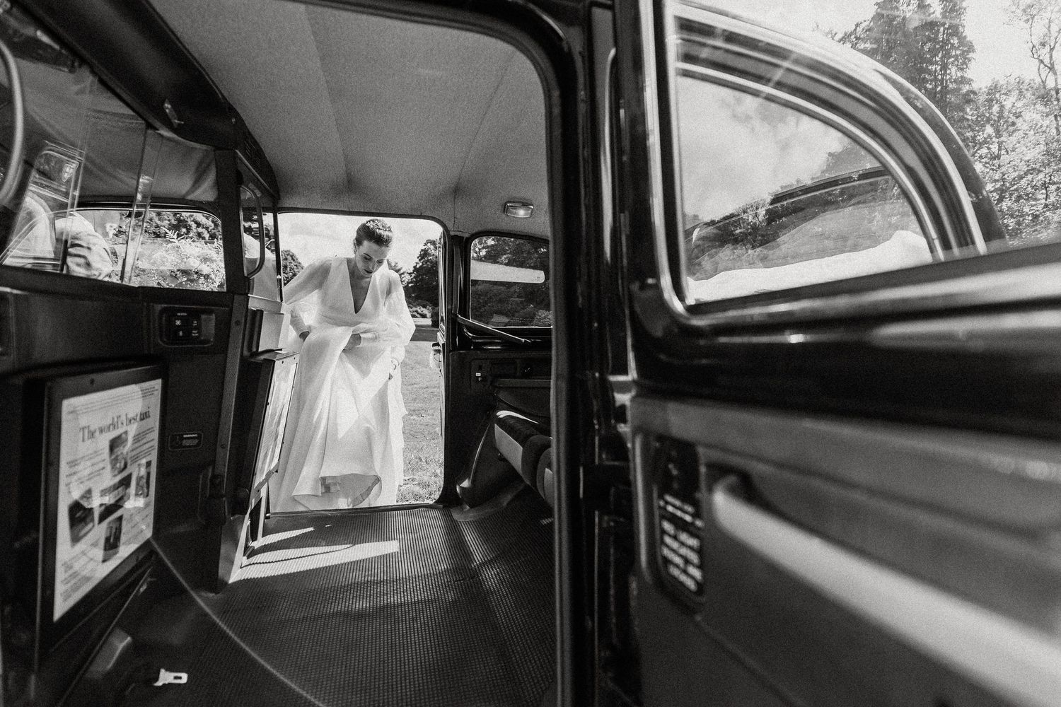 A black and white vintage wedding photo showing a couple through a car window as they prepare to depart.