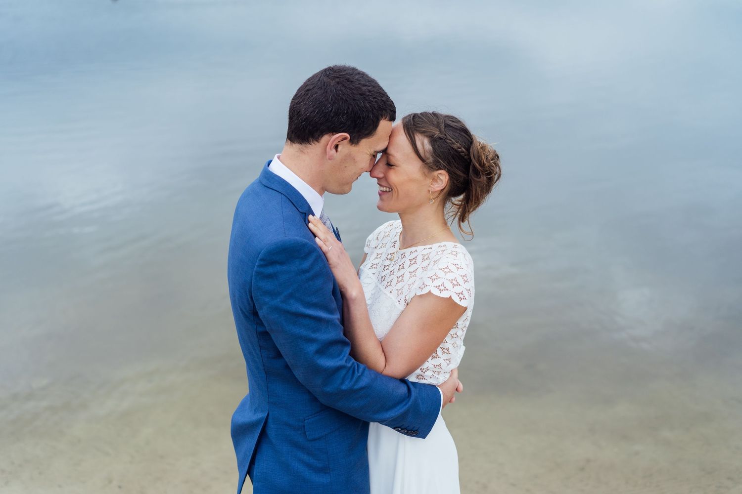 A couple in wedding attire shares an intimate moment by the water's edge on their special day.