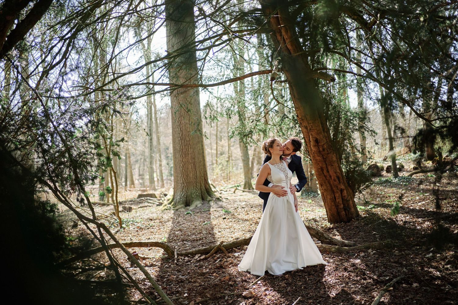 A couple shares romantic moments in a sunlit wooded forest setting during their wedding photoshoot.