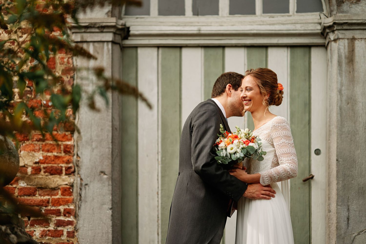 A romantic couple shares tender moments in front of a rustic brick wall and wooden door during their wedding photoshoot.