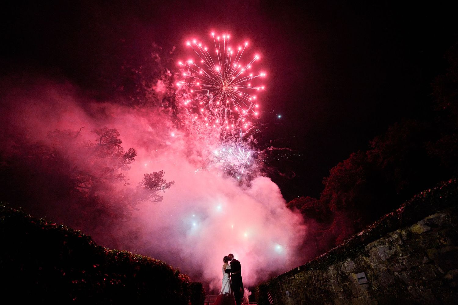 Silhouette of person watching pink fireworks explode against dark night sky during celebration display.