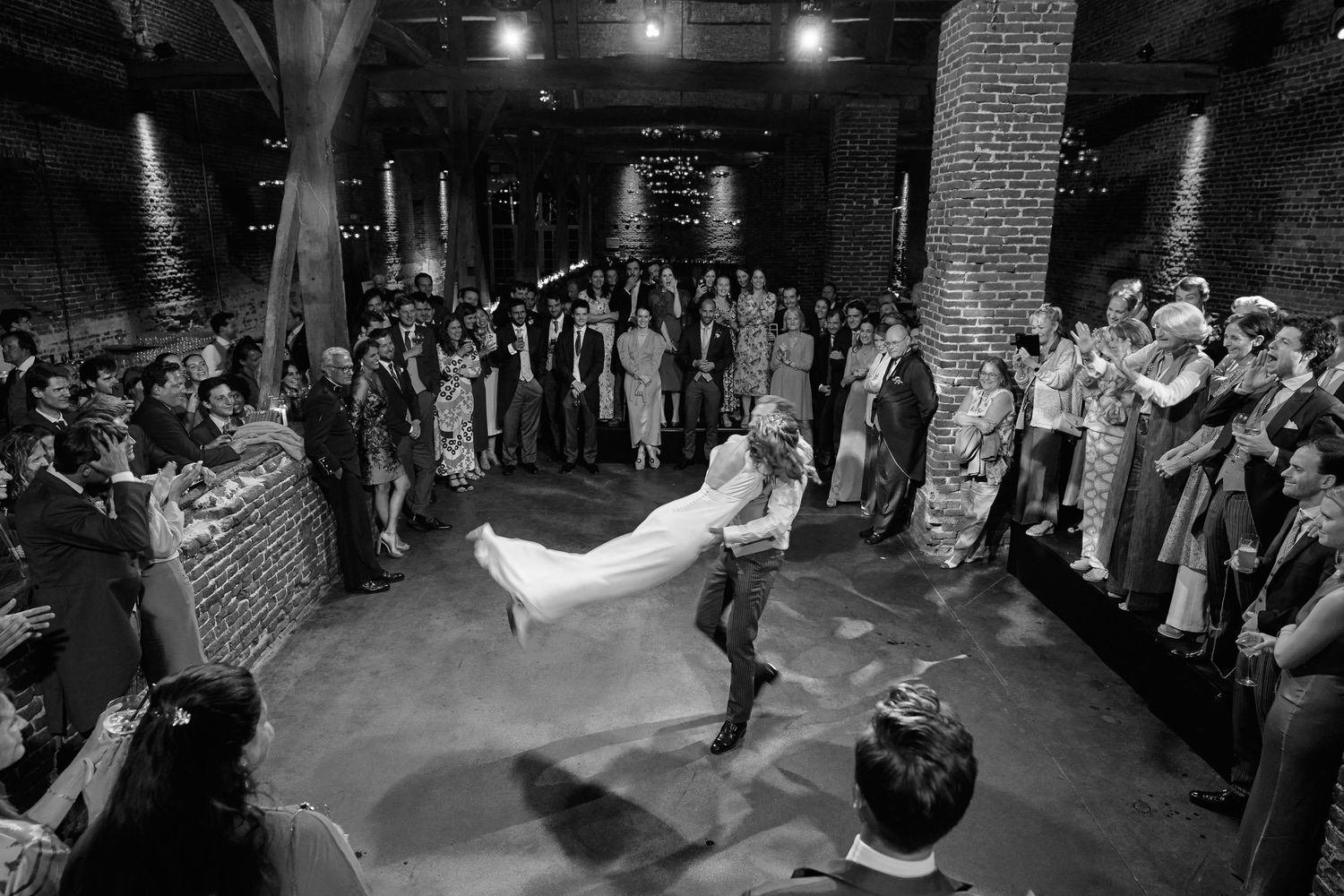 Black and white photos capture joyful moments during a wedding reception dance in an industrial brick venue.