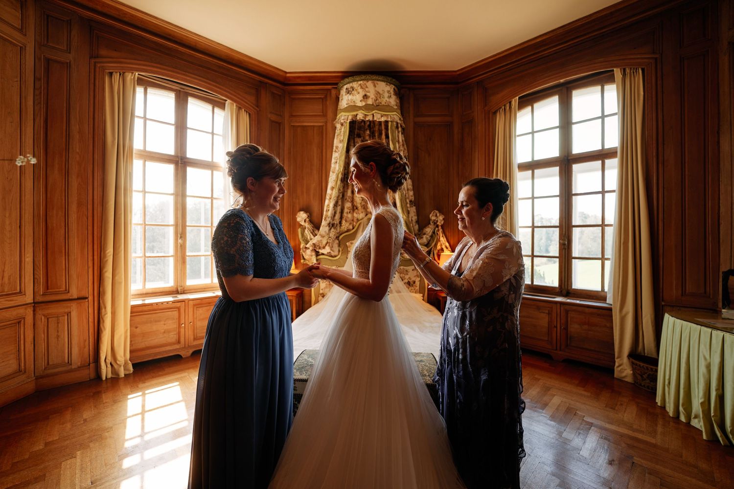 Sunlit wood-paneled room with large windows and flowing curtains creates an intimate wedding preparation space.