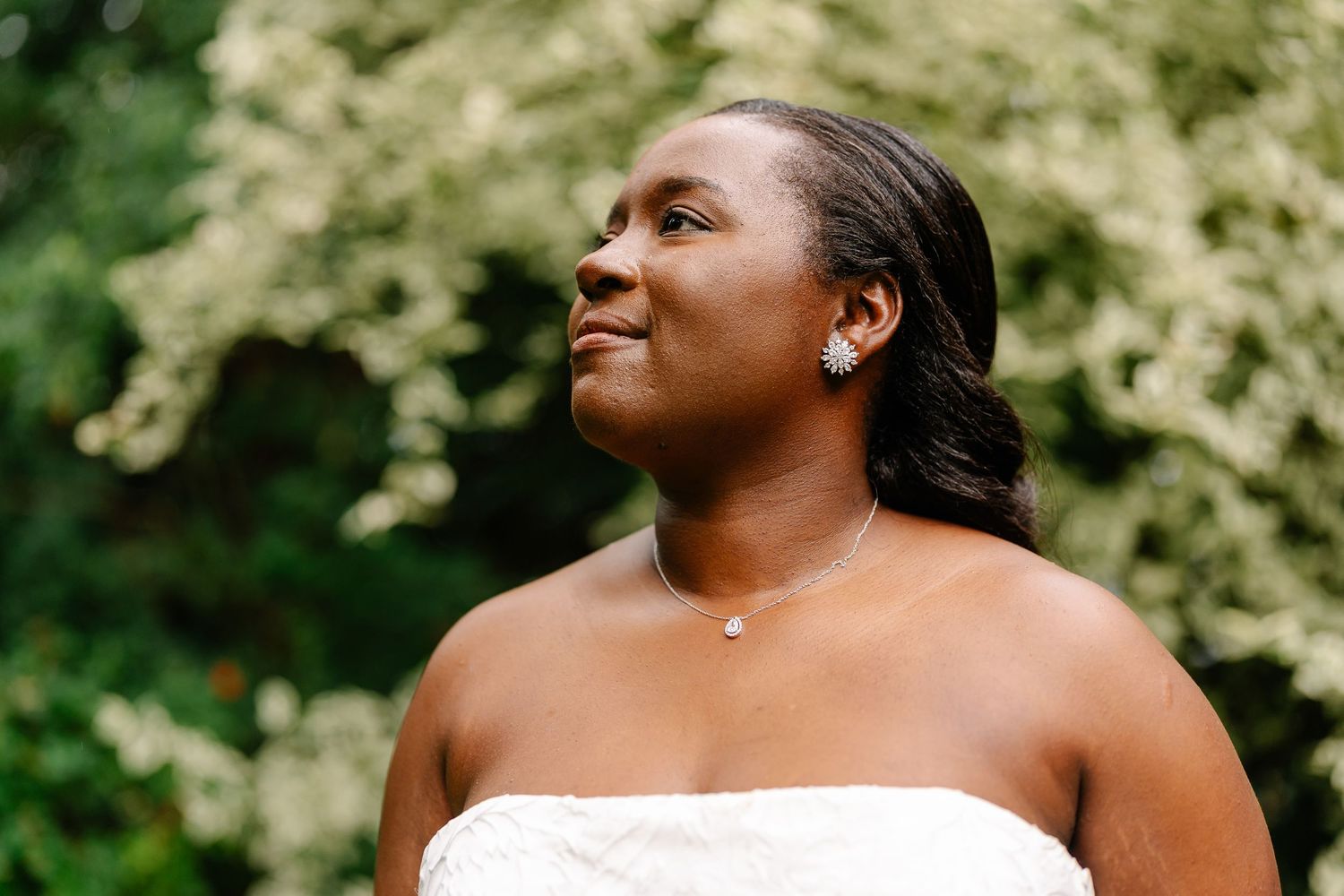 A person smiles joyfully in a garden setting with white flowering trees or bushes in the background.