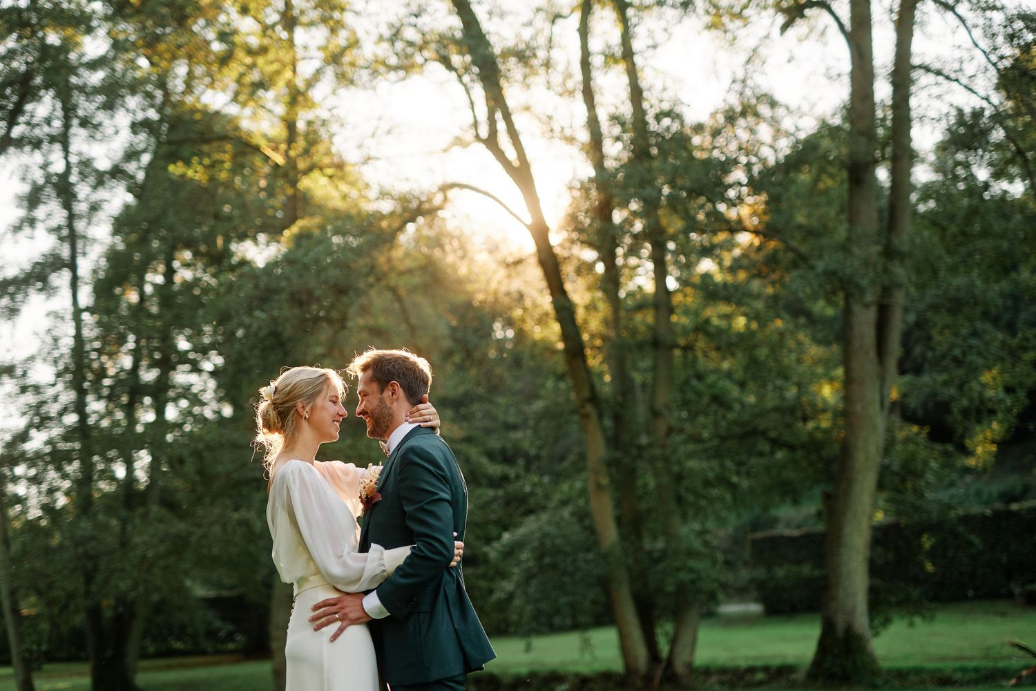 A couple shares a romantic embrace in a sunlit garden setting during their wedding celebration.