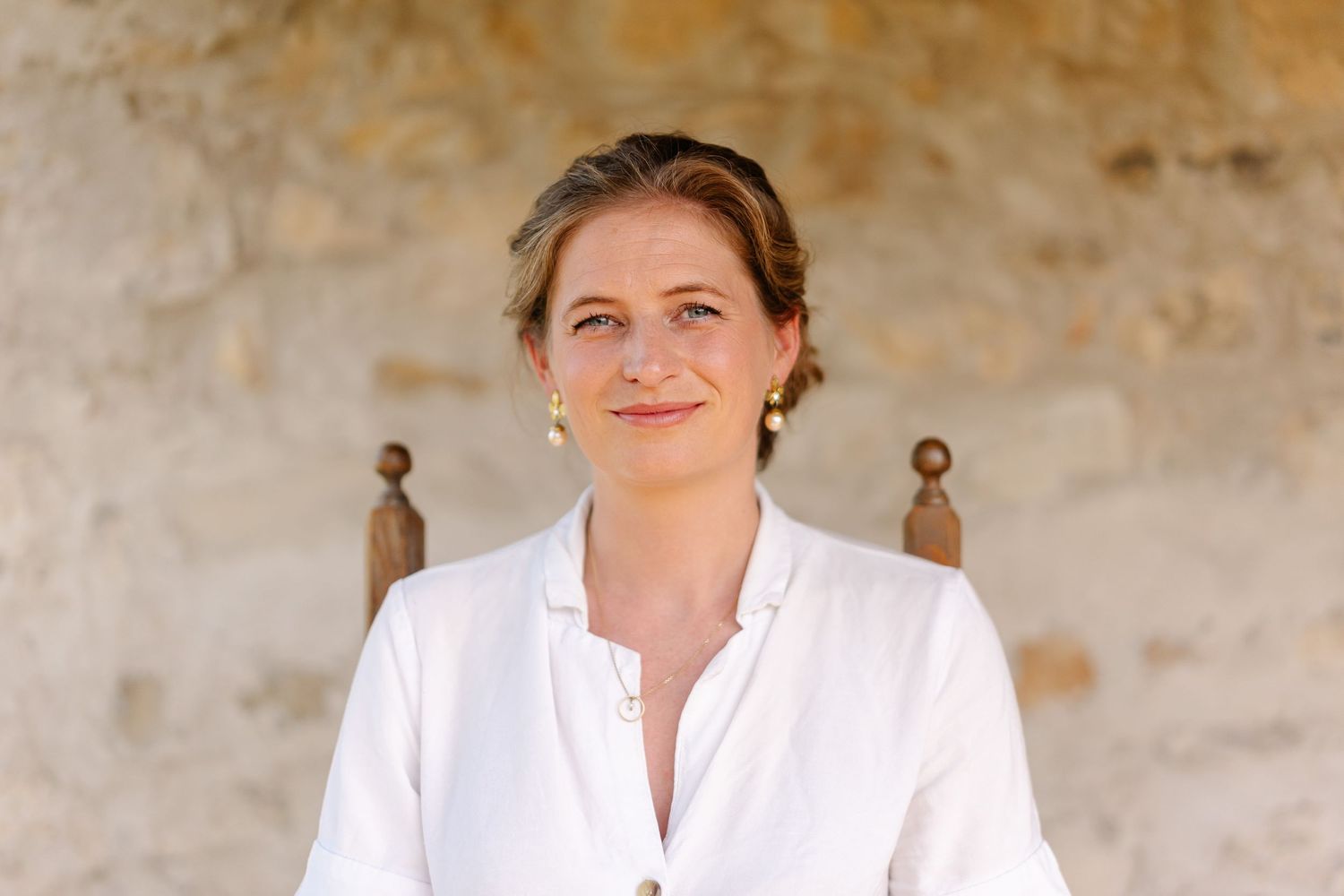 A person in a white dress smiles while sitting on a textured beige background.