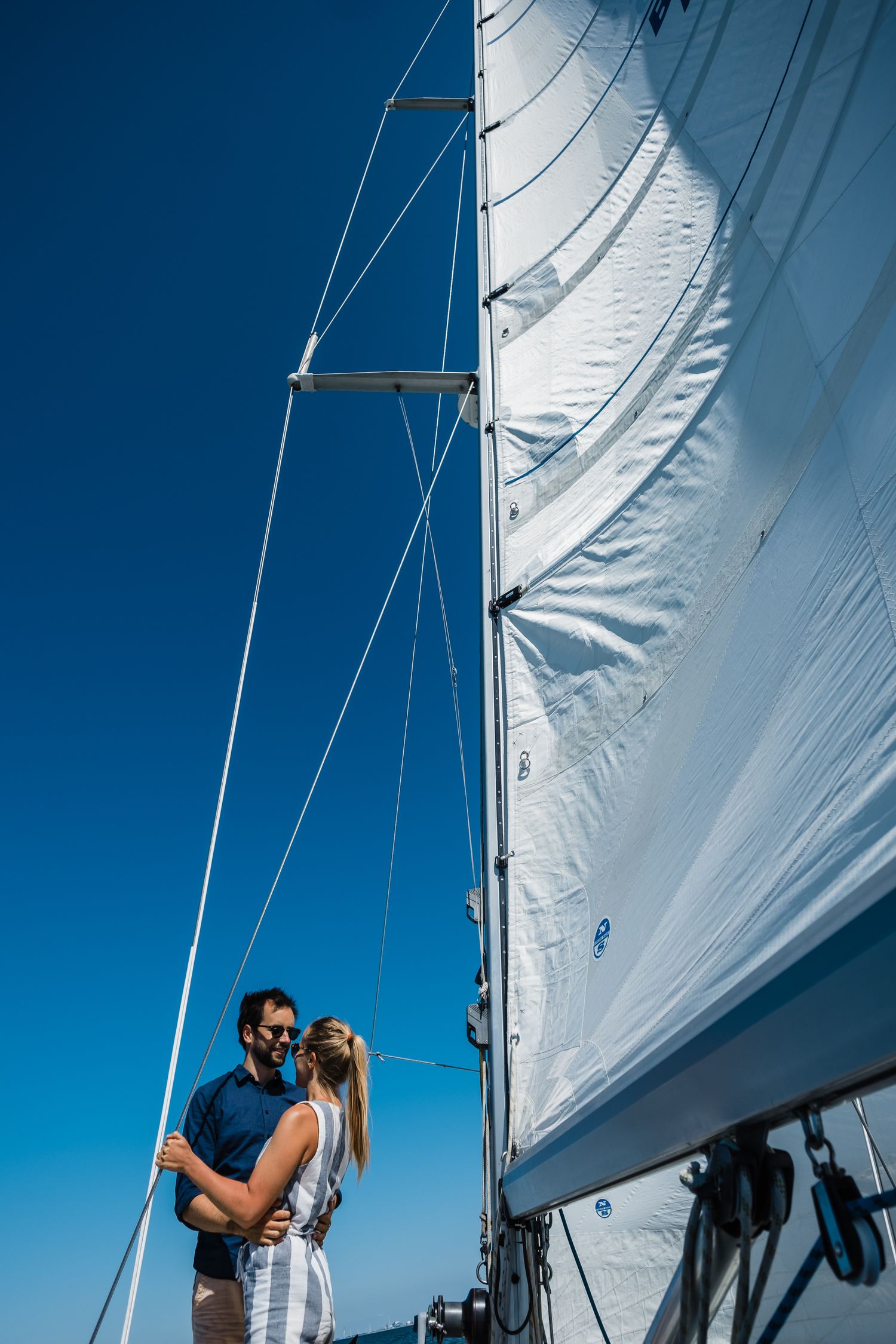 White sailboat sails billowing against a bright blue sky on a sunny day.