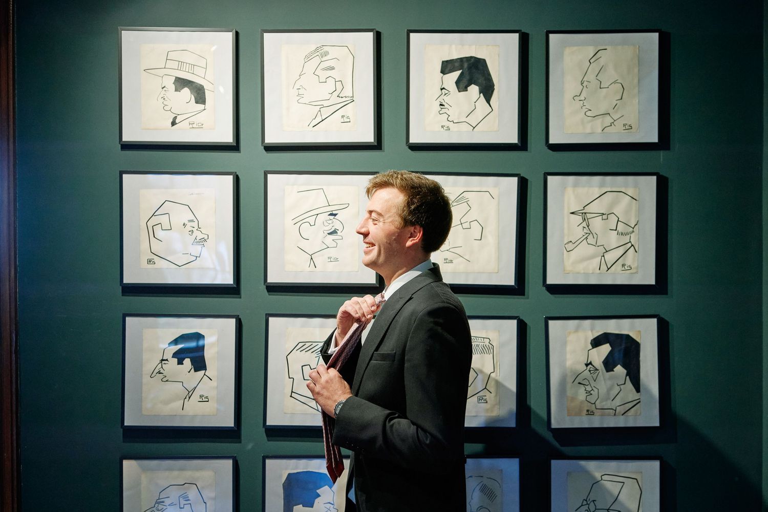 Art gallery wall displays multiple black and white portrait sketches in matching frames against a dark teal background.