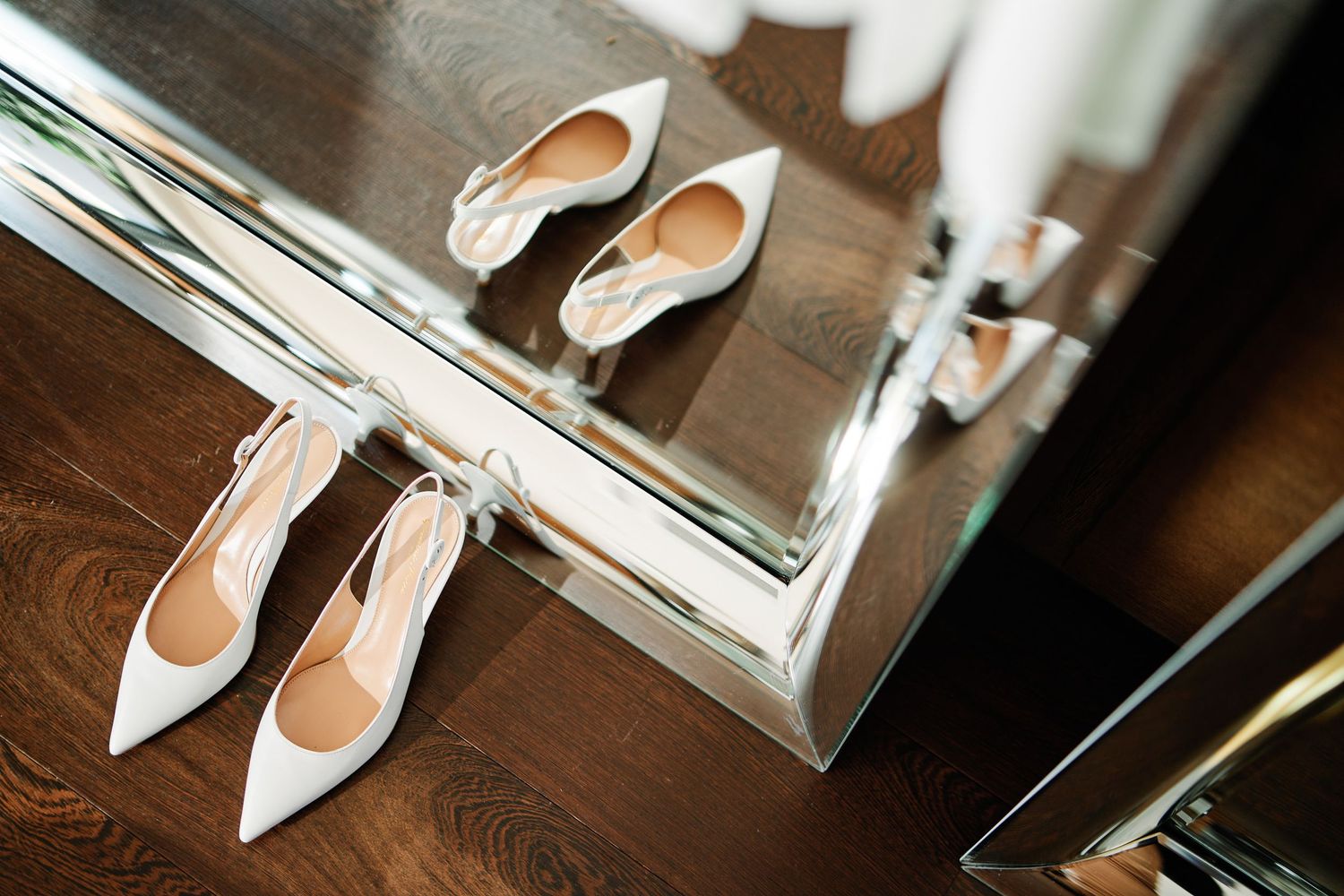 White leather stiletto heels arranged artistically with reflective mirror surfaces in an elegant display setting.