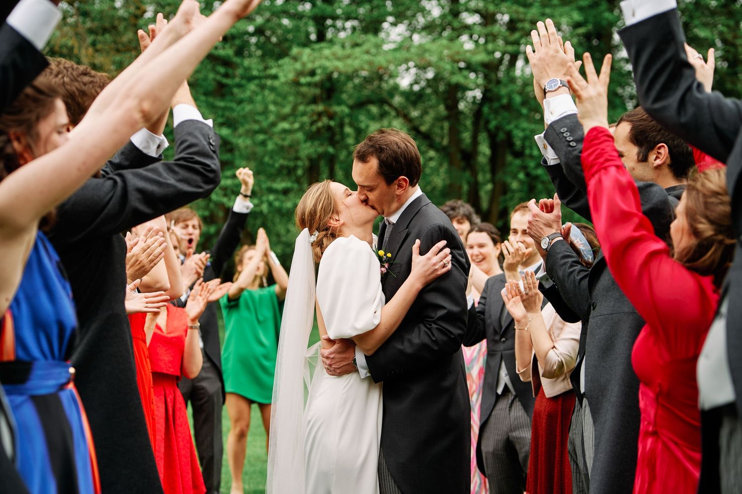 Wedding guests form a celebratory arch for the newlyweds to walk through in an outdoor garden setting.