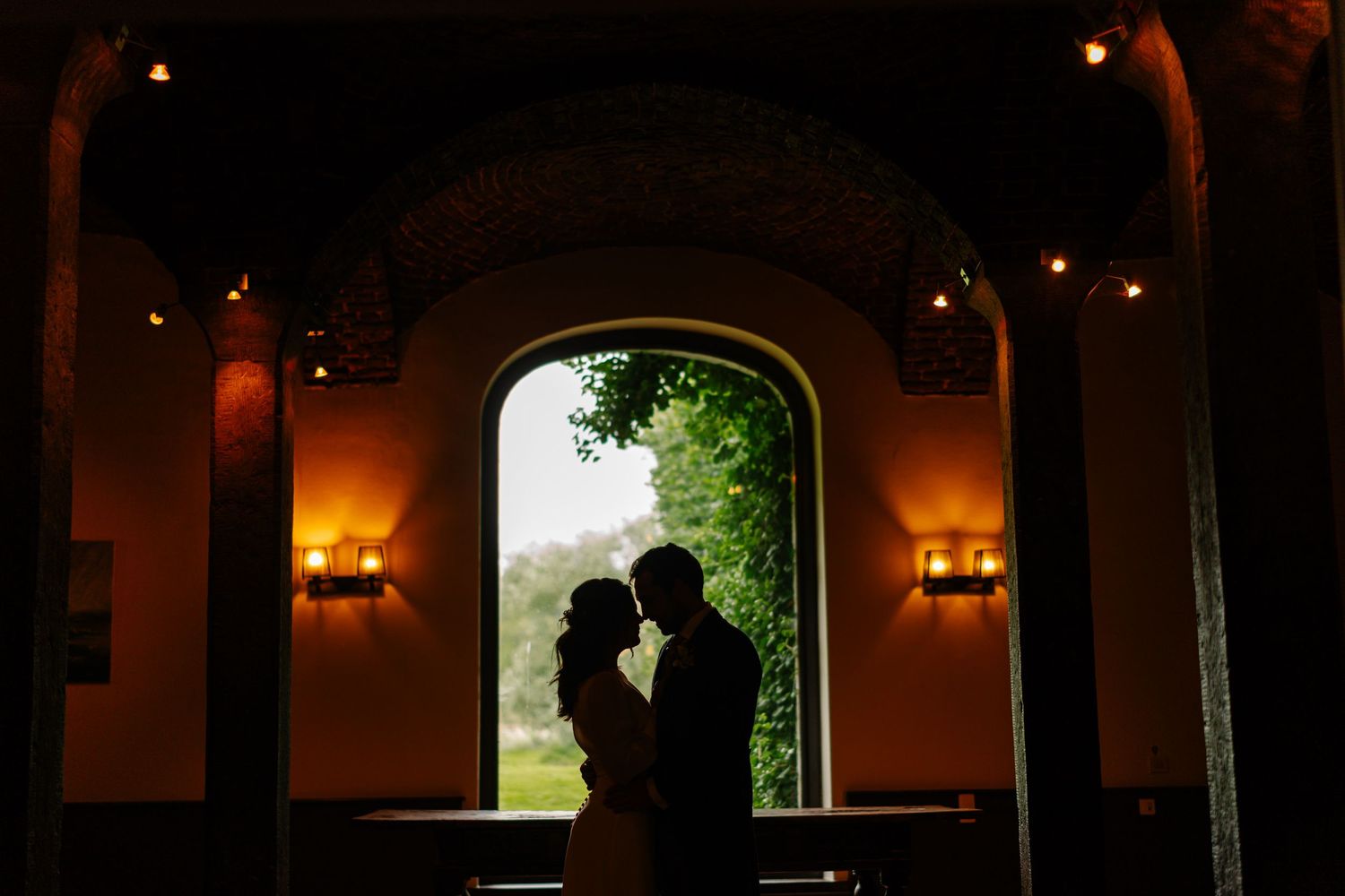Romantic silhouettes of a couple in an arched doorway at dusk with warm glowing lights in the background.