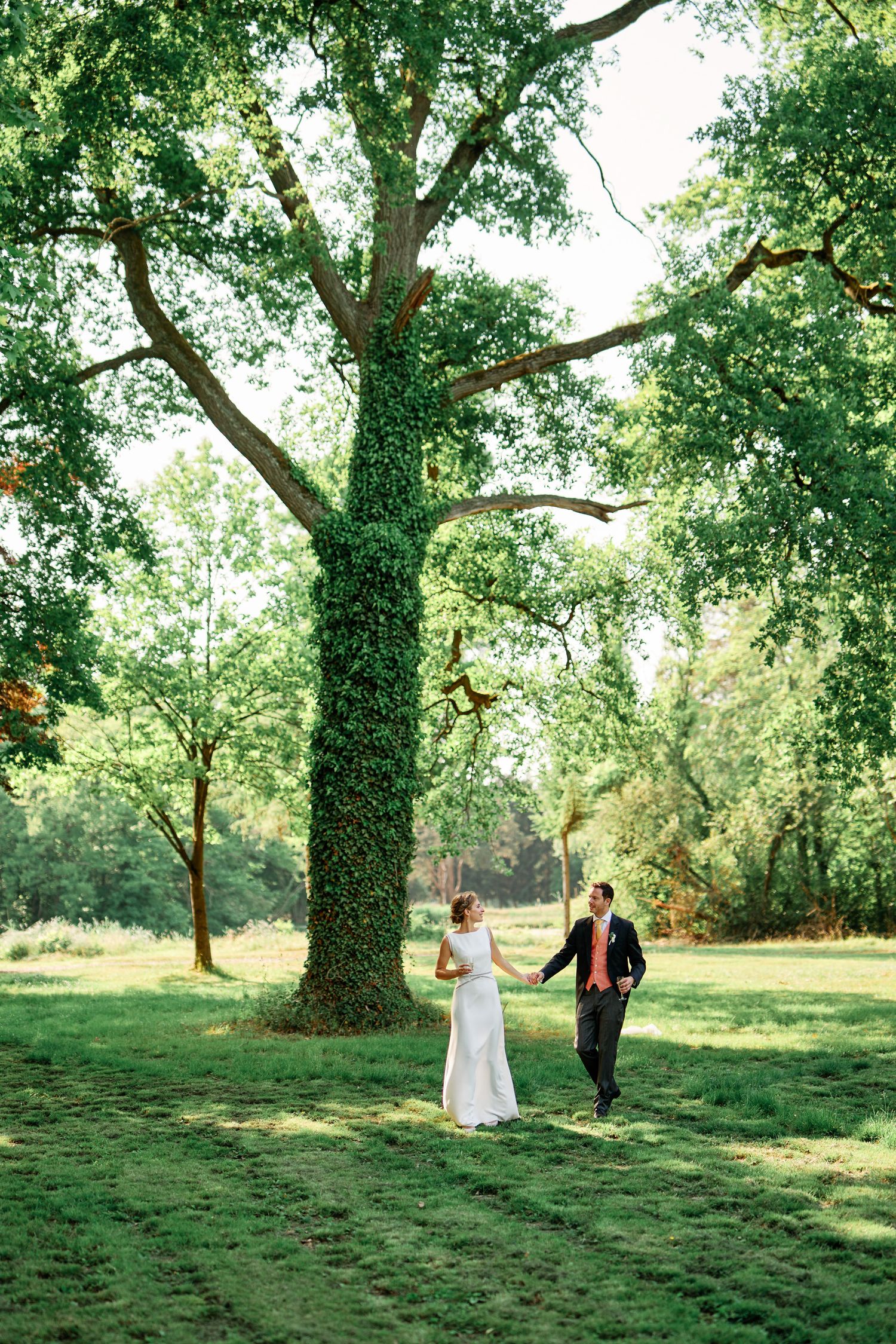 A couple walks through a lush green garden with ivy-covered trees creating a romantic natural setting.