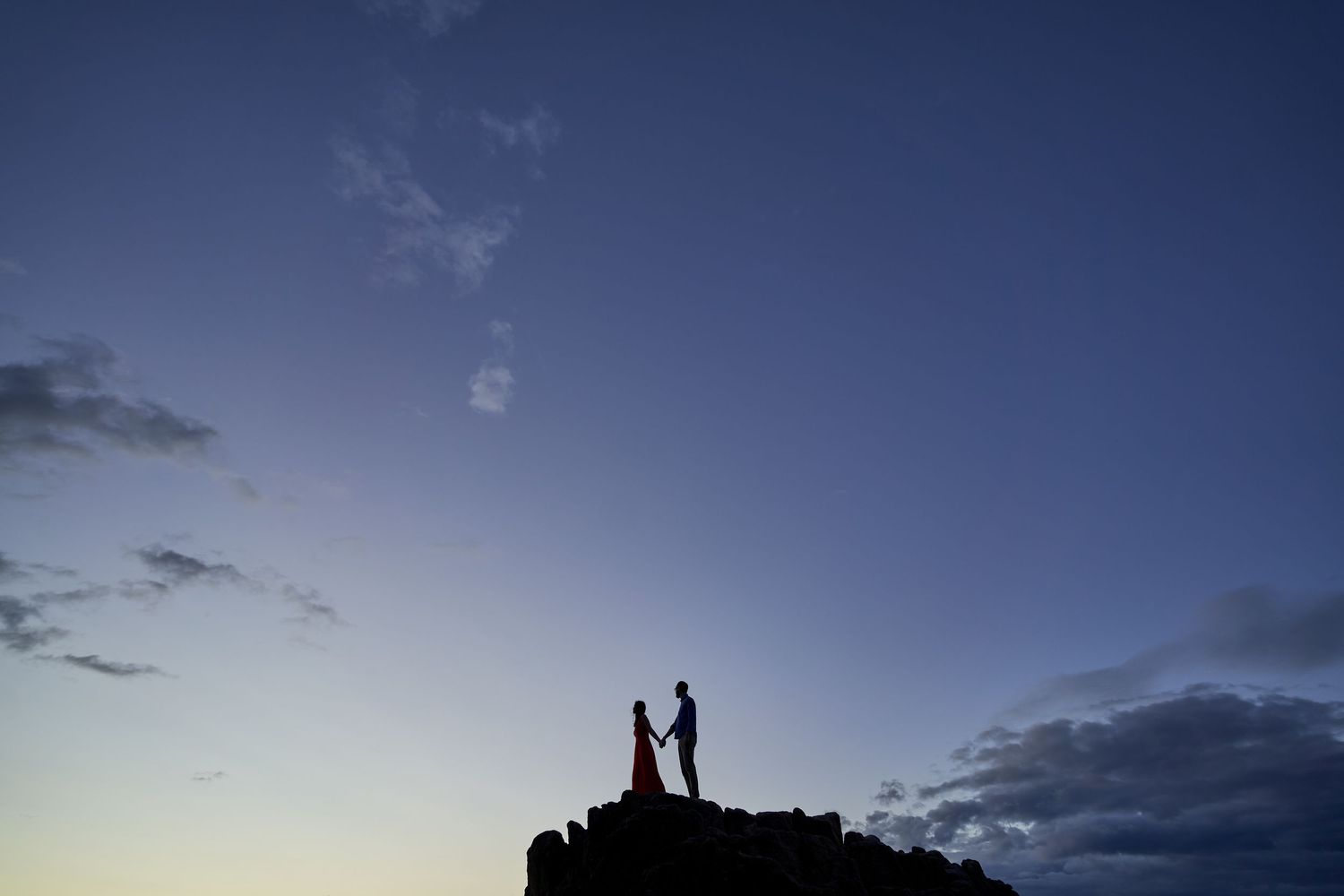 Silhouettes of people standing against a dramatic sunset sky with clouds in the background.