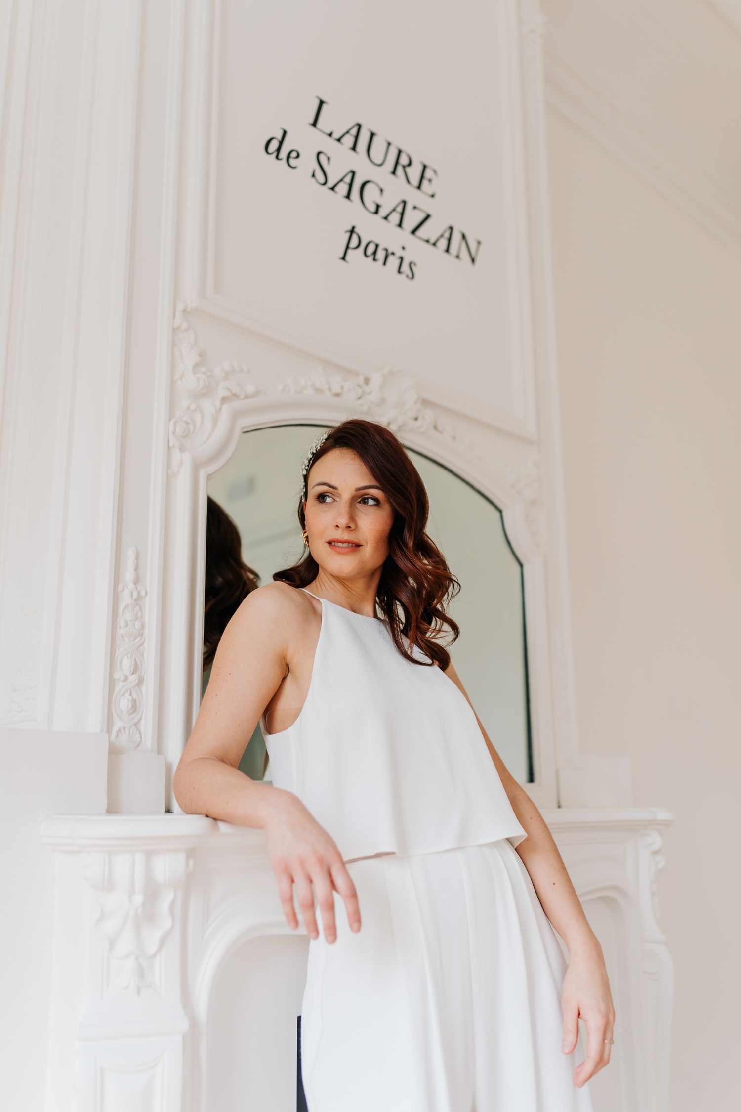 Elegant white two-piece bridal ensemble shown in a luxurious Parisian setting with ornate moldings and Laure de Sagazan branding.