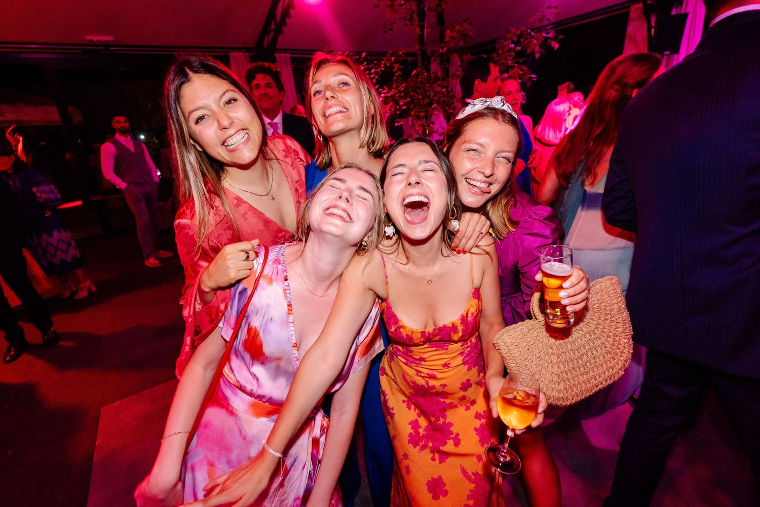People dancing and celebrating at a nightclub with vibrant pink and red lighting creating an energetic party atmosphere.