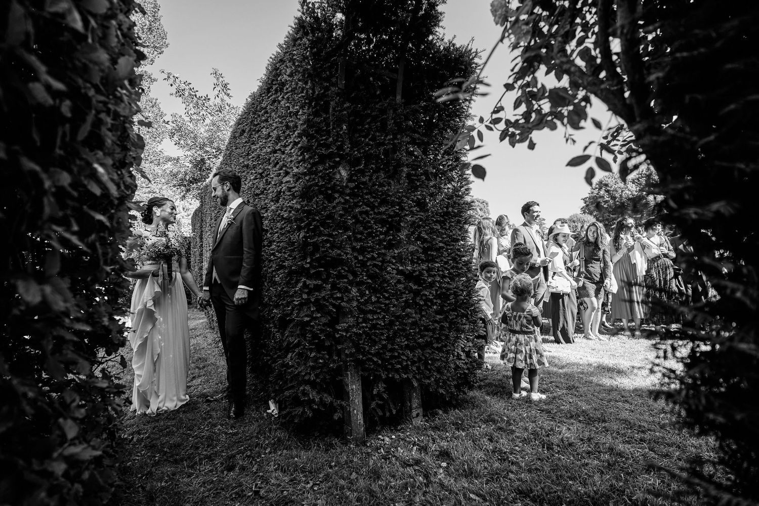 A series of black and white photographs showing people walking along garden paths and hedgerows.