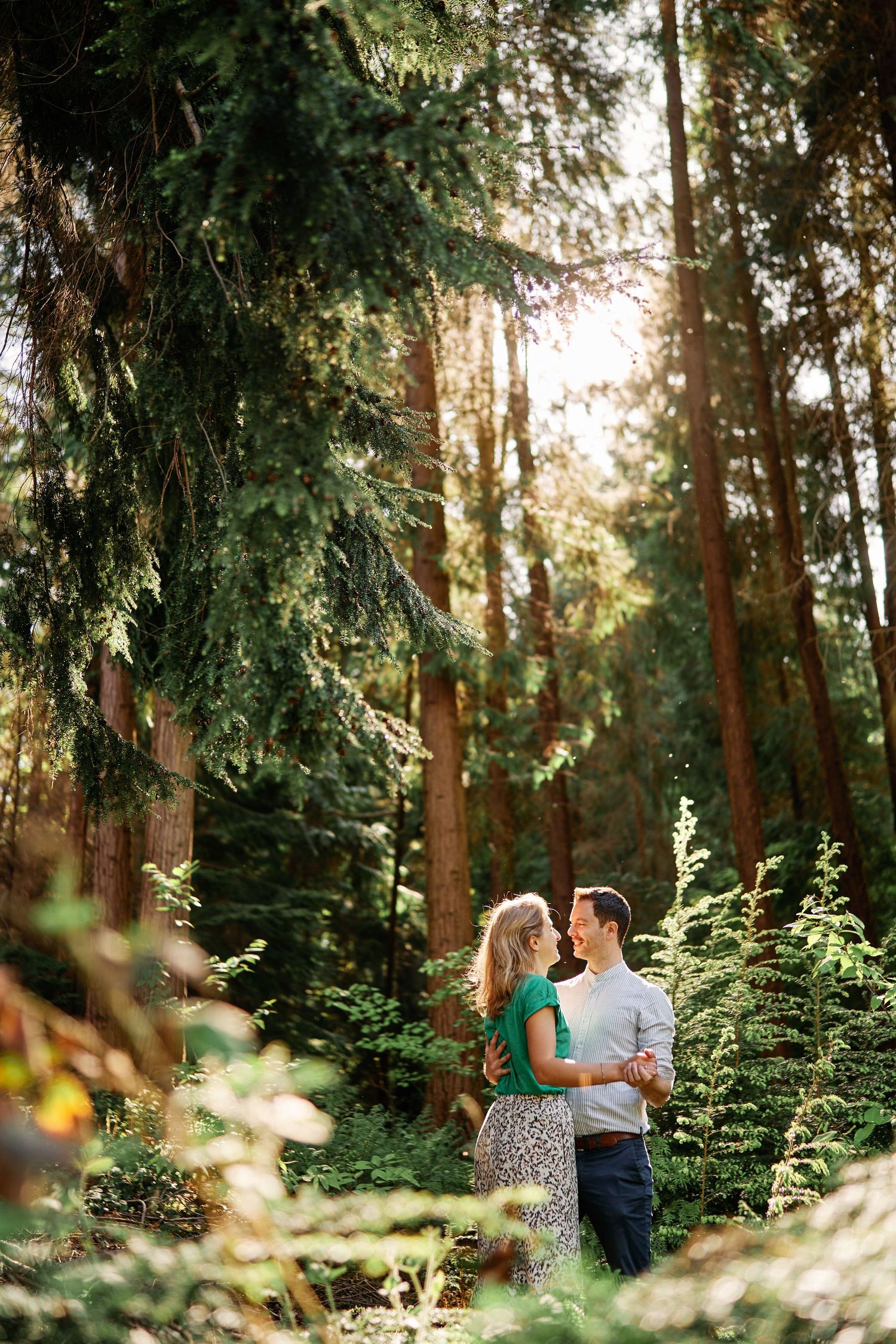 A couple shares an intimate moment in a lush green forest setting during golden hour.