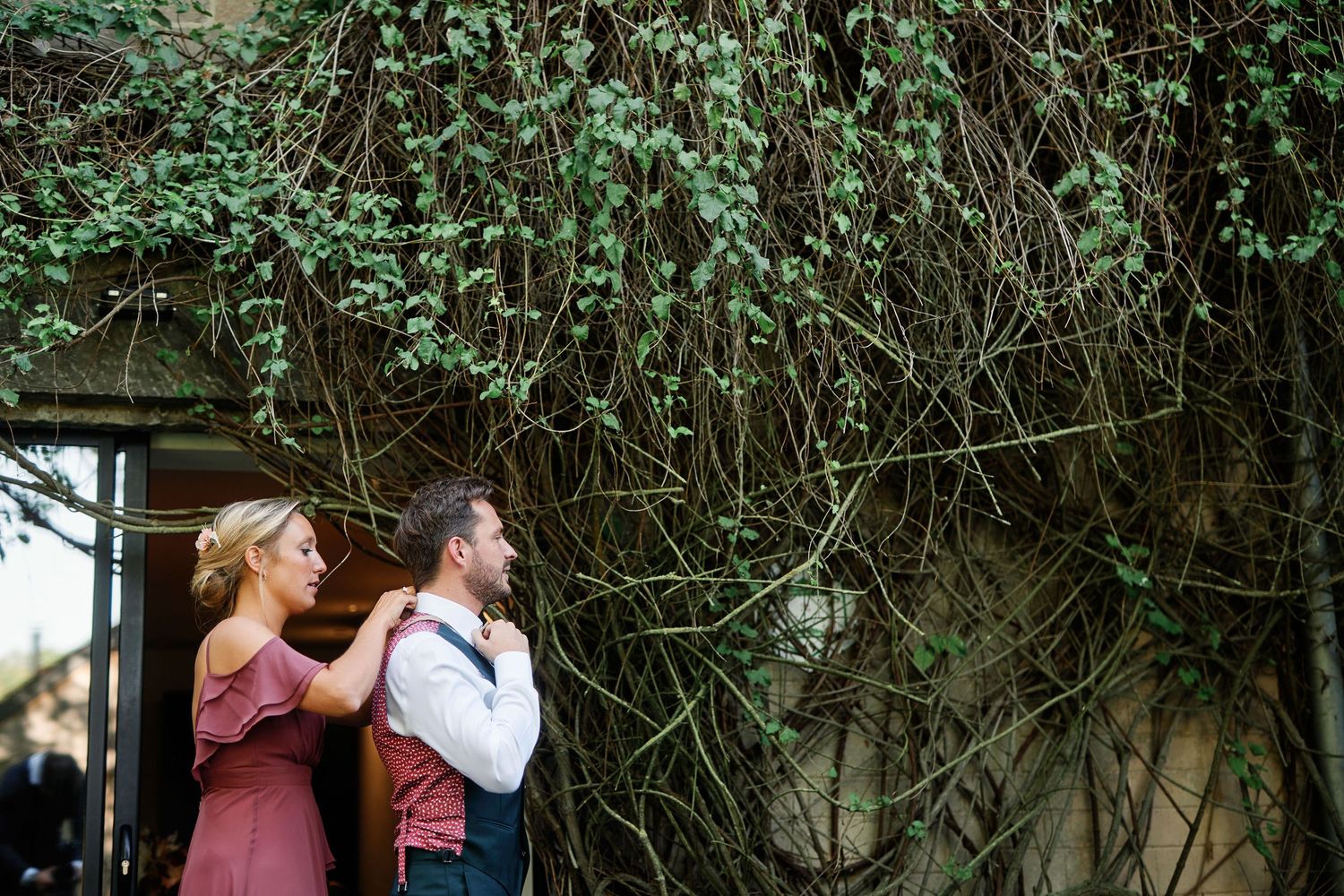 Couple shares a tender moment together against a wall covered in lush green vines and foliage.