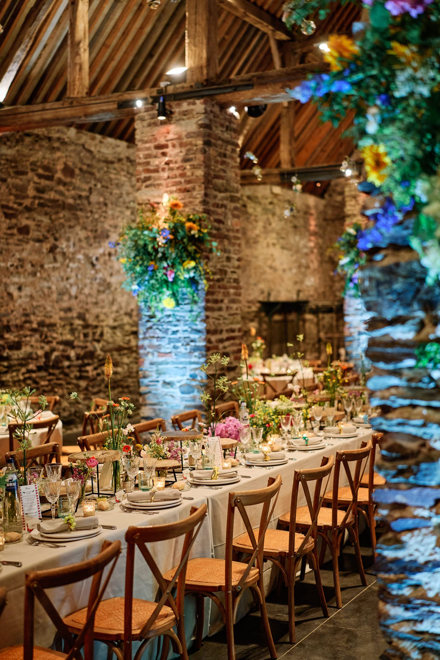 Rustic stone barn wedding reception venue with elegant table settings and blue uplighting on exposed brick walls.
